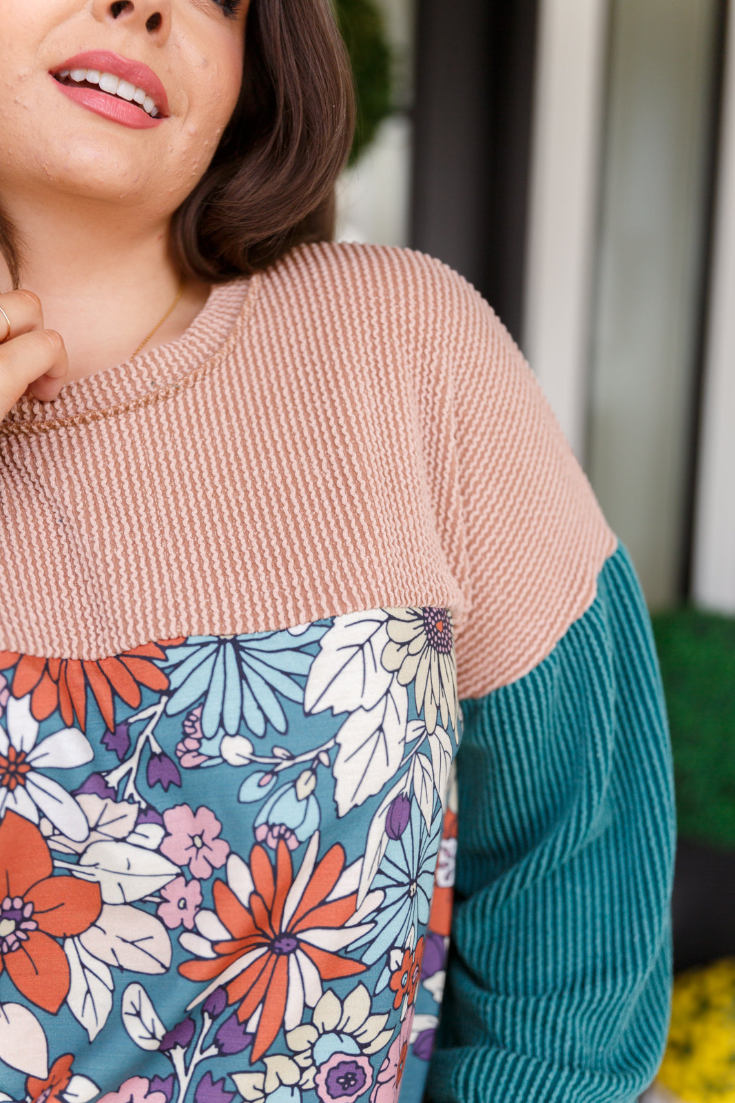 Close-up of woman wearing color block top with ribbed blush and teal sleeves and vibrant floral print front panel