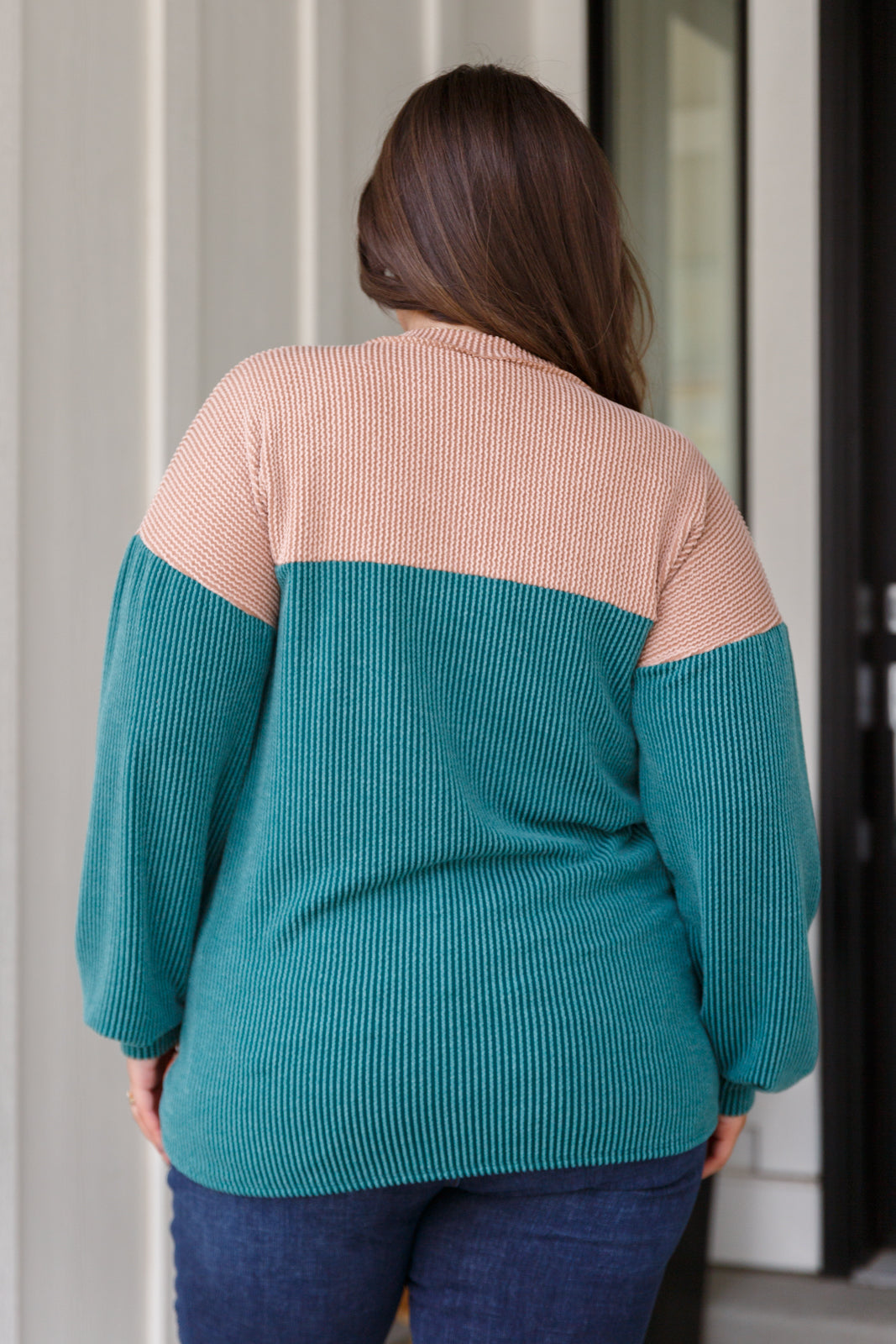 Woman wearing teal and blush color block ribbed top with long sleeves shown from back indoors