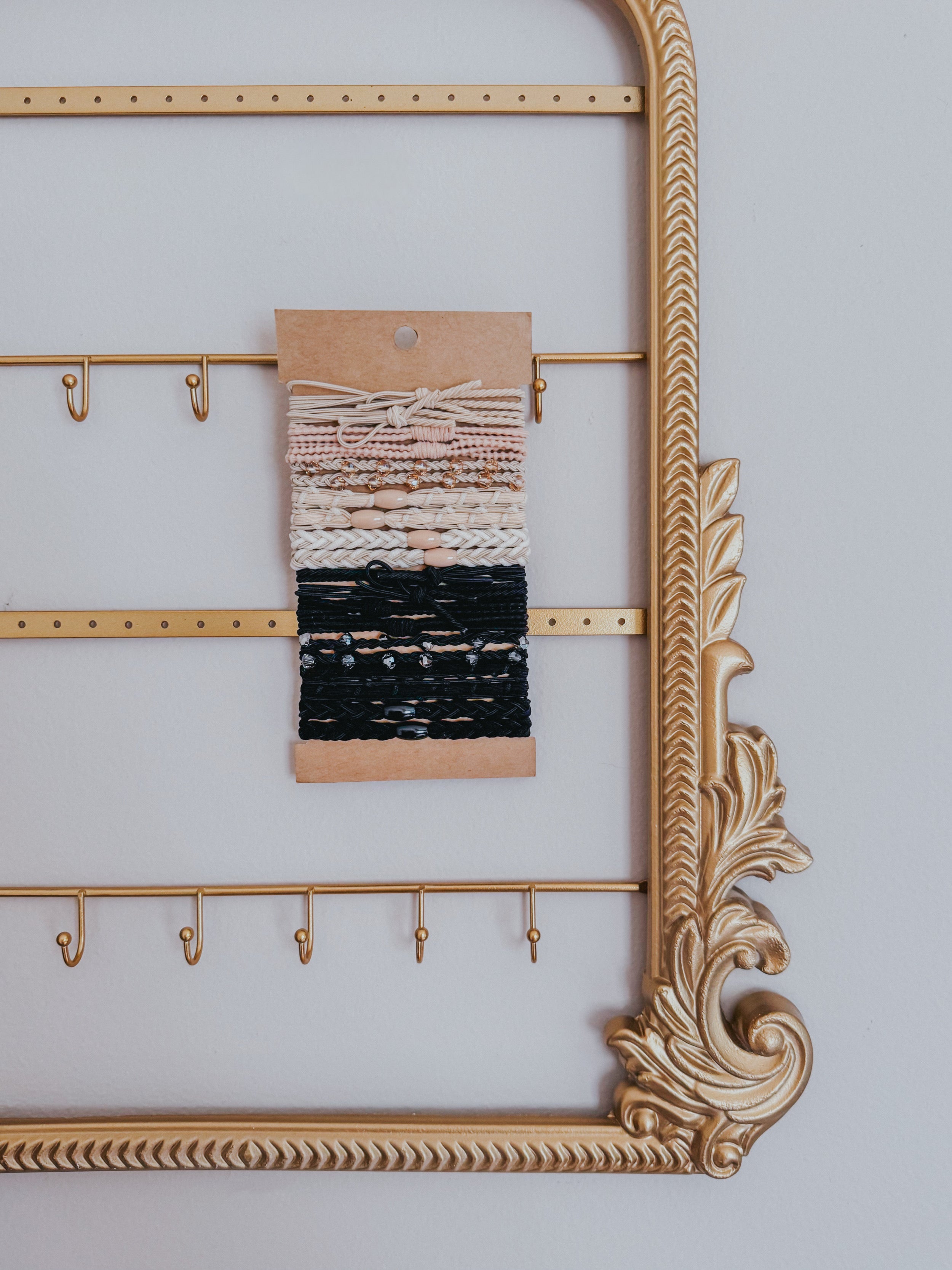 Set of cream and black woven stackable hair tie bracelets displayed on kraft card within decorative gold frame accessory holder
