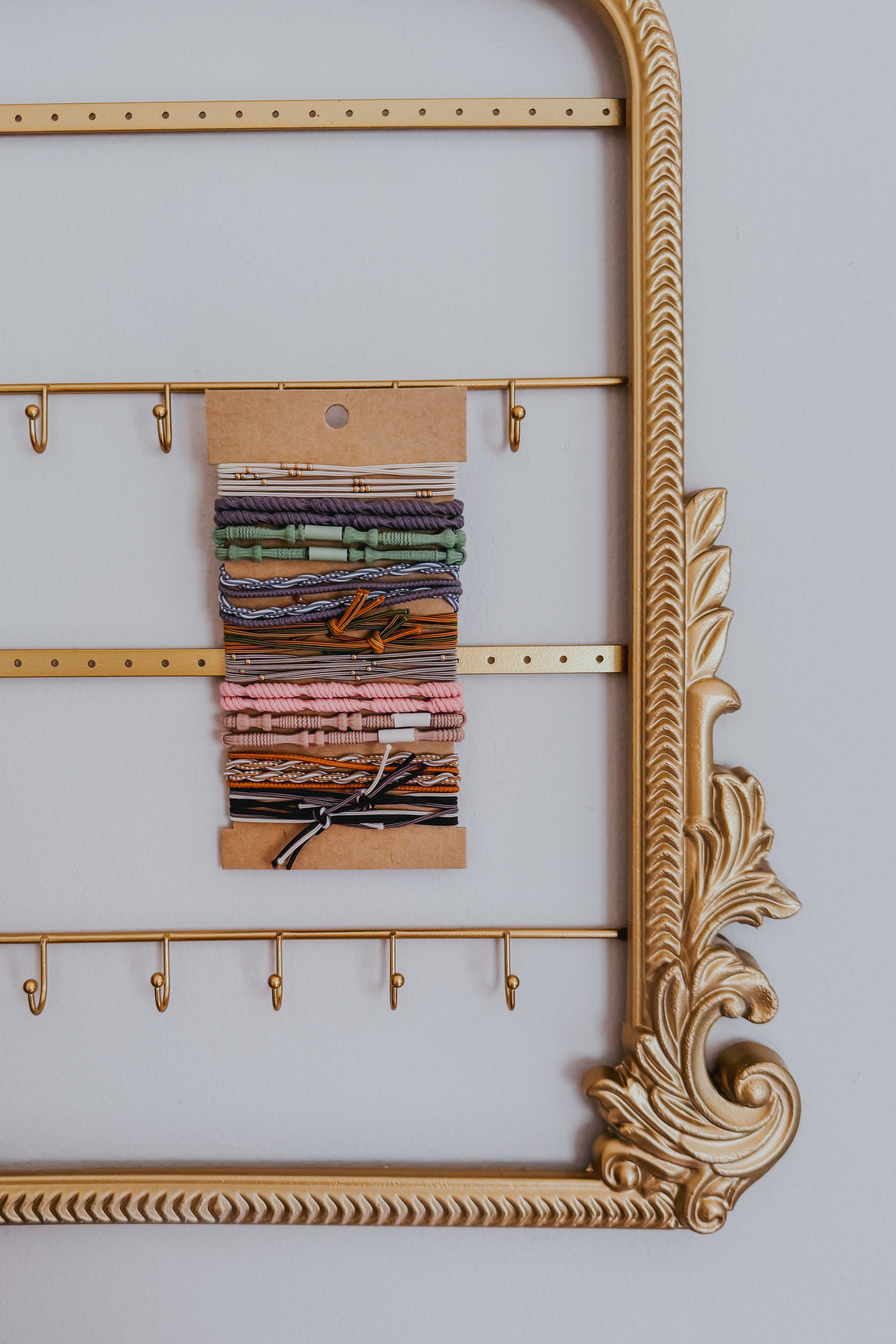 Set of earth tone stackable hair ties and bracelets with knotted and braided details on kraft card in decorative gold frame