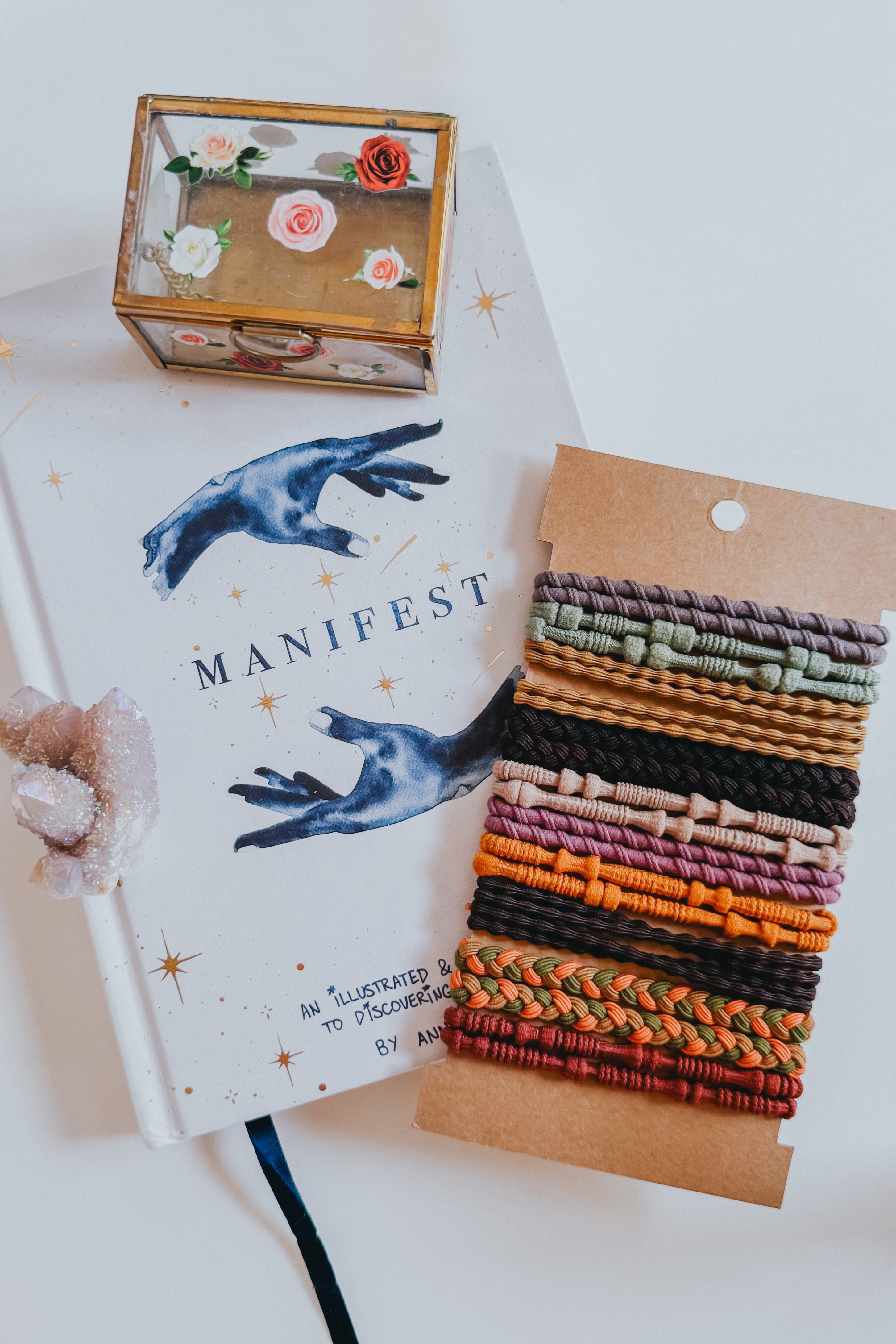Set of textured stackable hair tie bracelets in warm earthy and muted sunset tones on kraft card backing next to a manifest journal