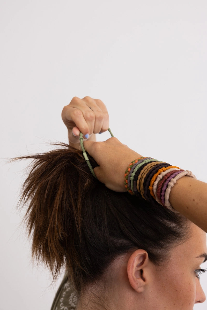 Wrist adorned with vibrant sunset-hued stackable hair tie bracelets while securing hair in a casual updo.