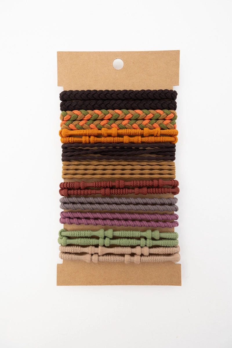 Collection of stackable hair tie bracelets in sunset-inspired warm tones with braided and twisted details on kraft card backing