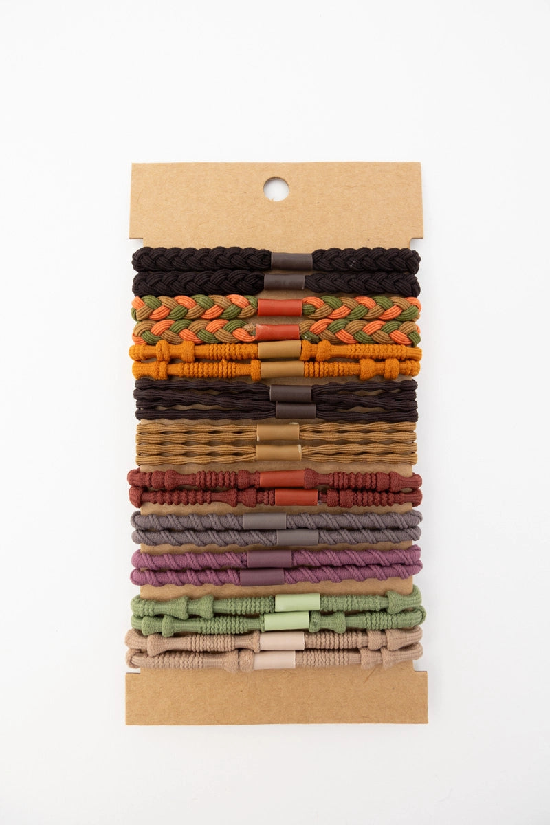 Set of varied stackable hair ties in warm sunset-inspired shades with mixed braided and knotted textures on kraft card backing