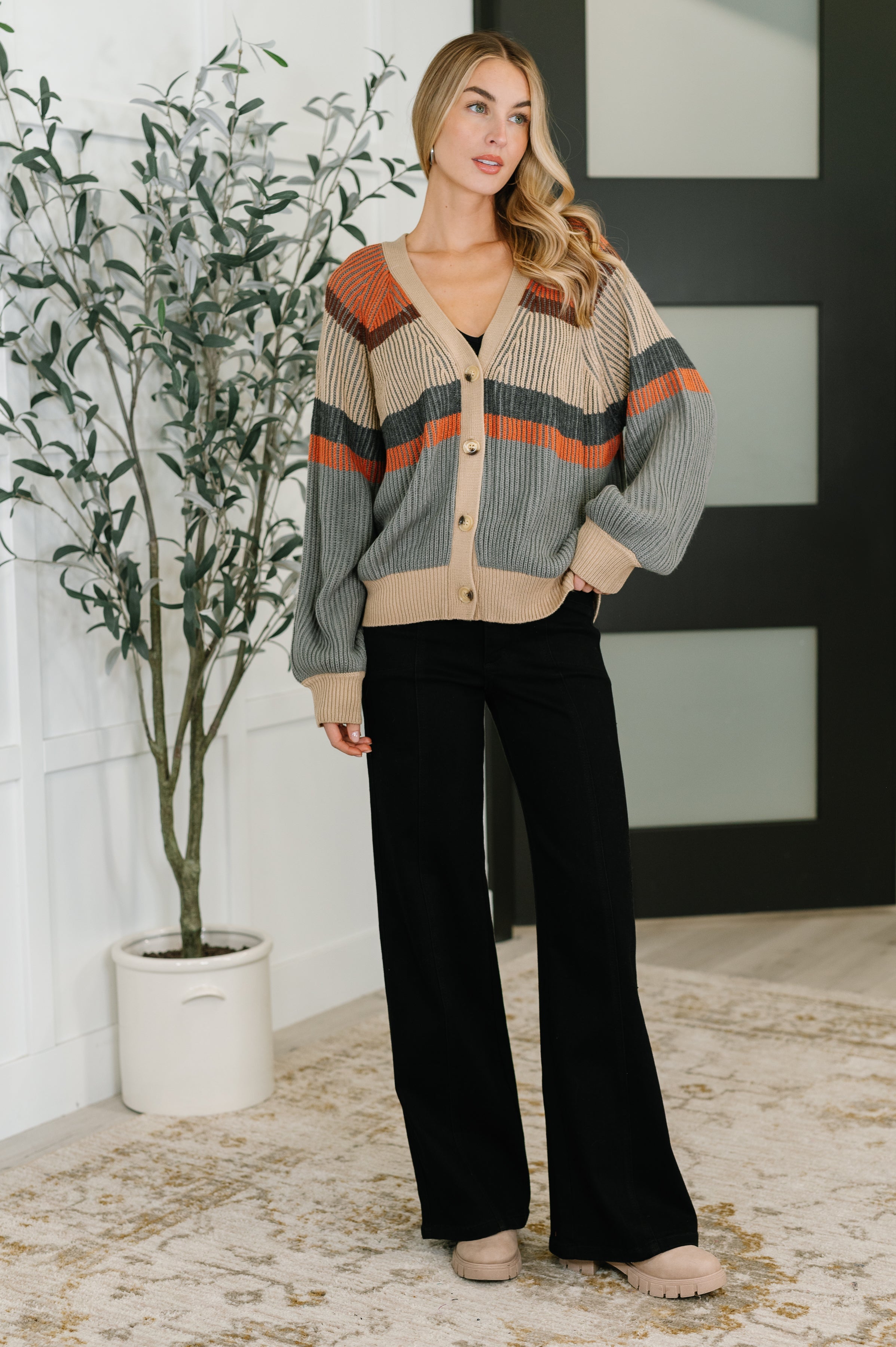 Woman wearing tan and rust striped relaxed knit cardigan paired with black wide-leg pants indoors