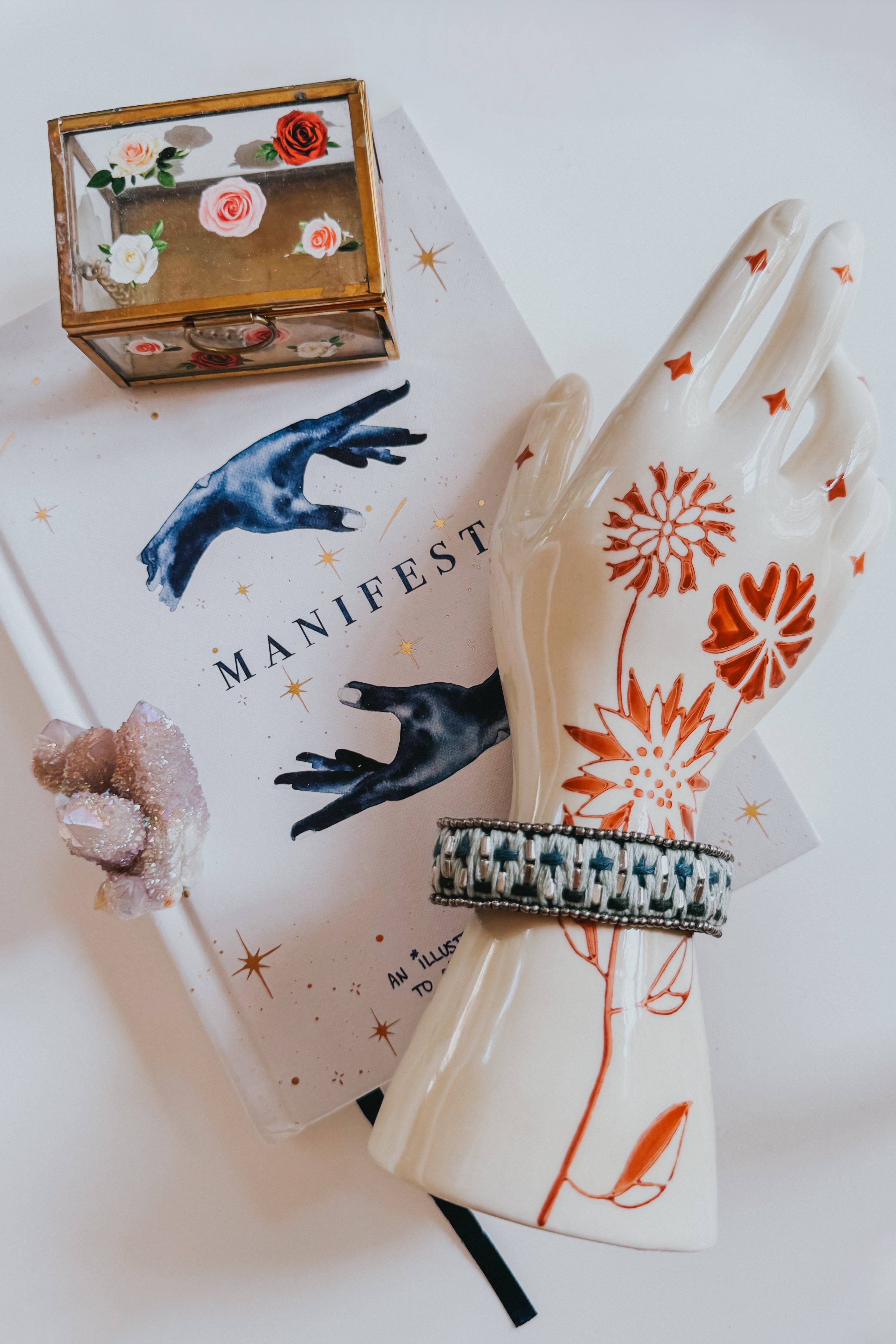 Blue woven velvet bracelet with snap closure displayed on ceramic hand with red floral details atop a Manifest journal