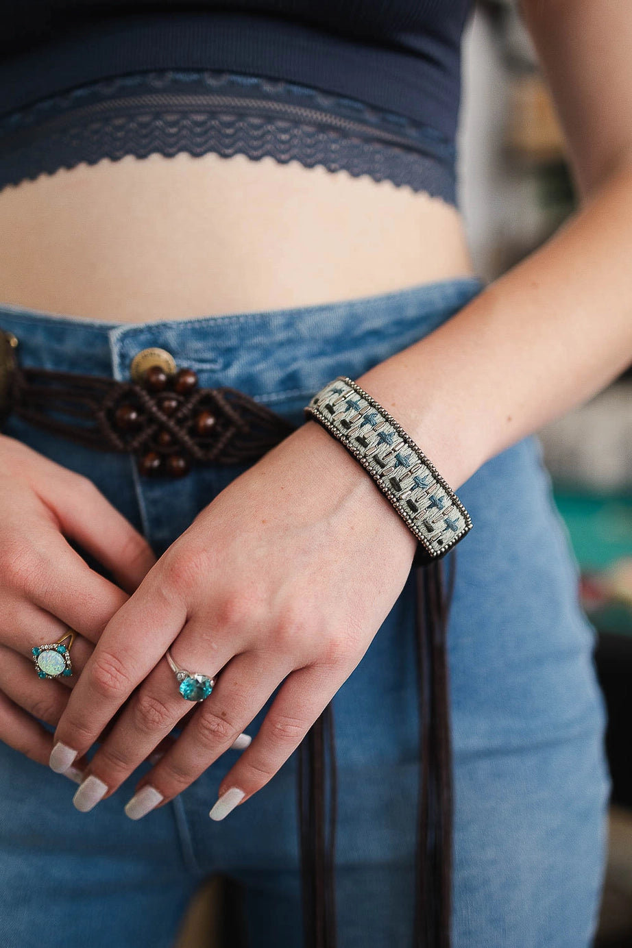 Close-up of wrist wearing blue woven velvet snap bracelet paired with turquoise rings and casual denim outfit