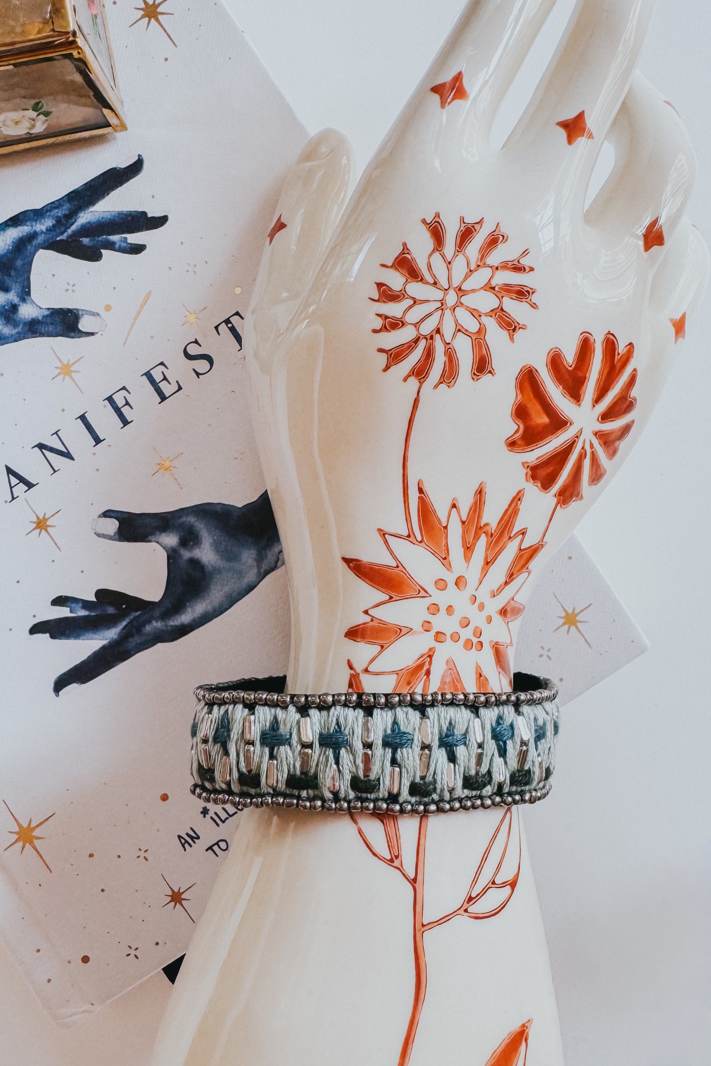 Woven velvet snap bracelet with blue and cream thread displayed on decorative ceramic hand on Manifest journal