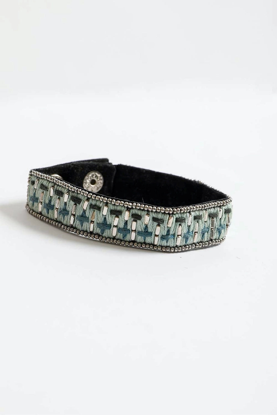 Woven velvet snap bracelet in shades of blue and silver with detailed bead trim on black backing against white background