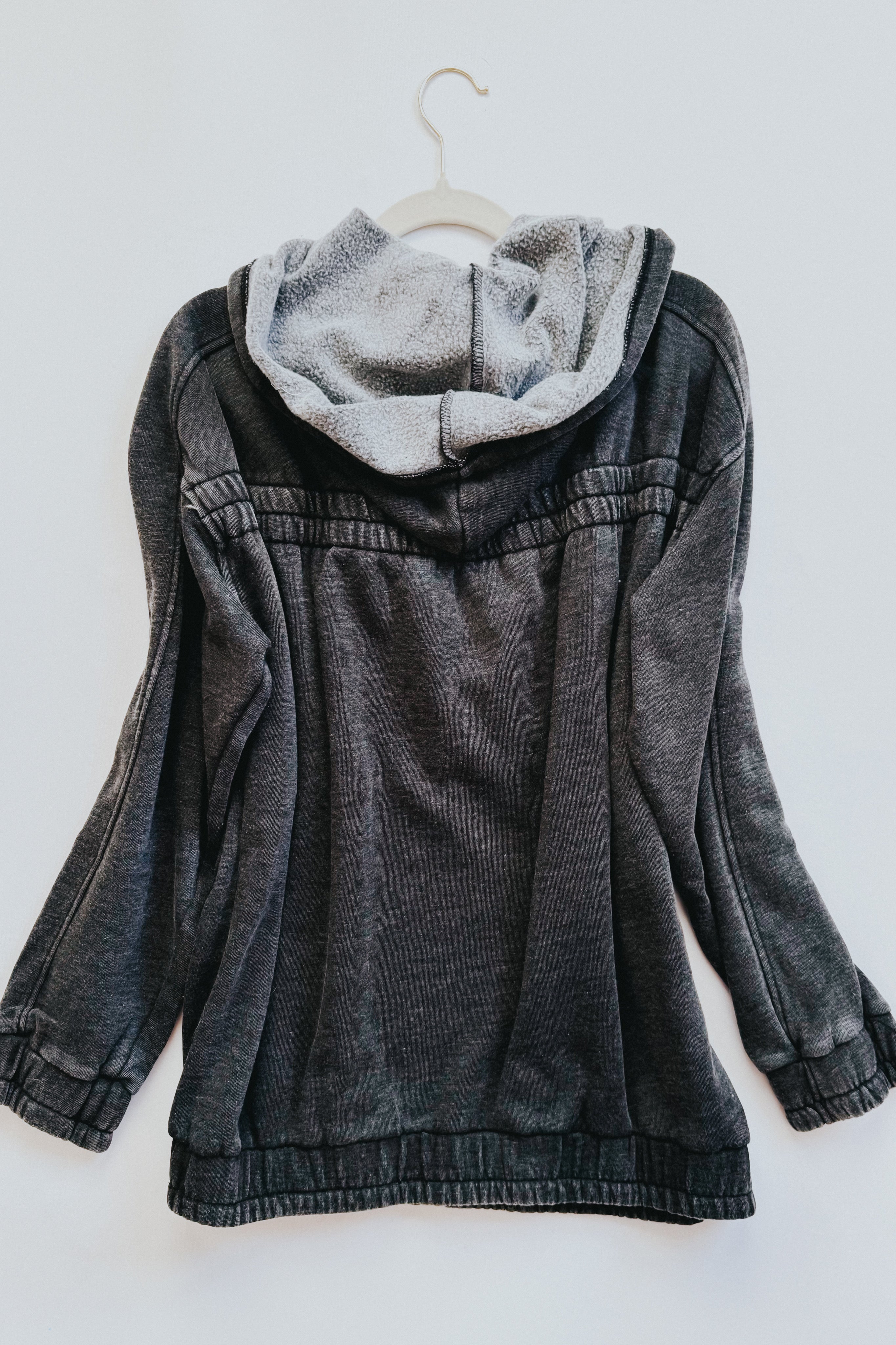 Charcoal acid wash hoodie hanging on white hanger showing plush lined hood and gathered cuffs and hem