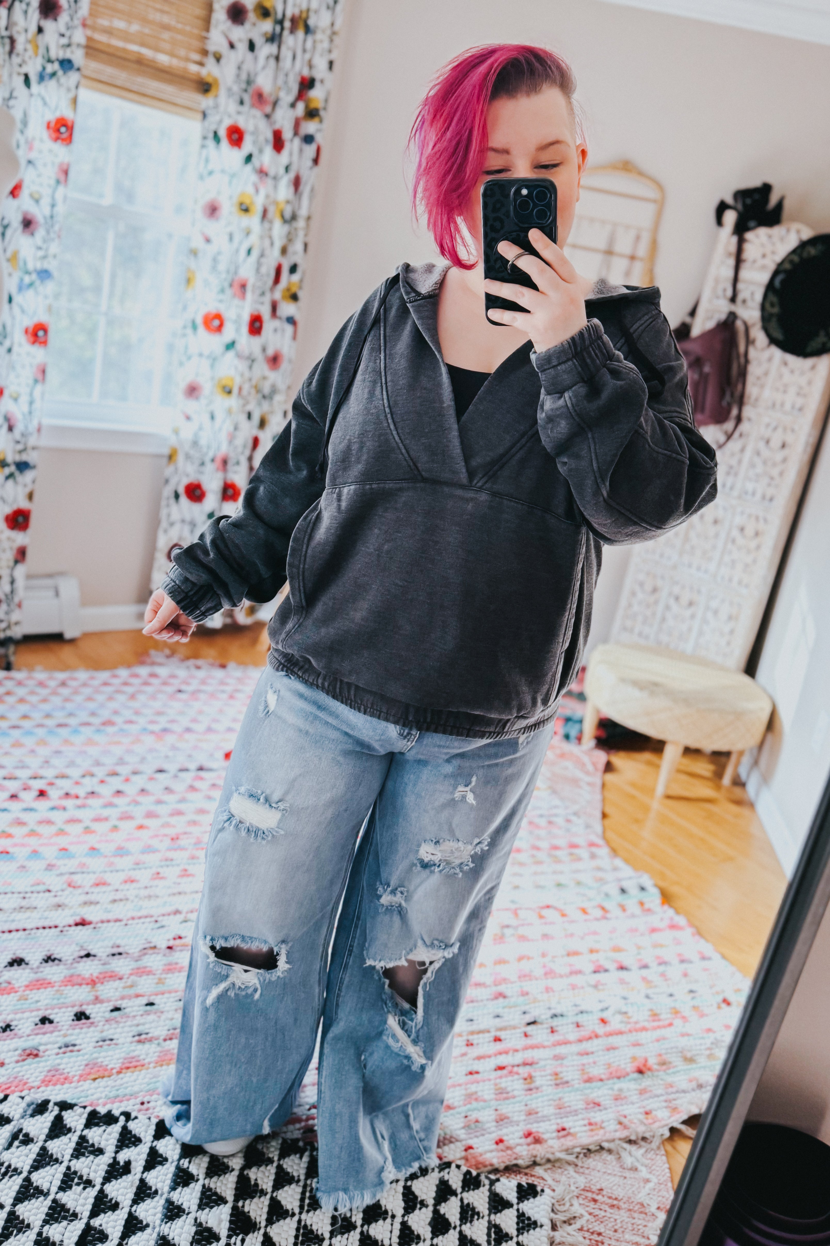 Woman with pink hair wearing charcoal acid wash hoodie and ripped wide-leg jeans taking a mirror selfie indoors