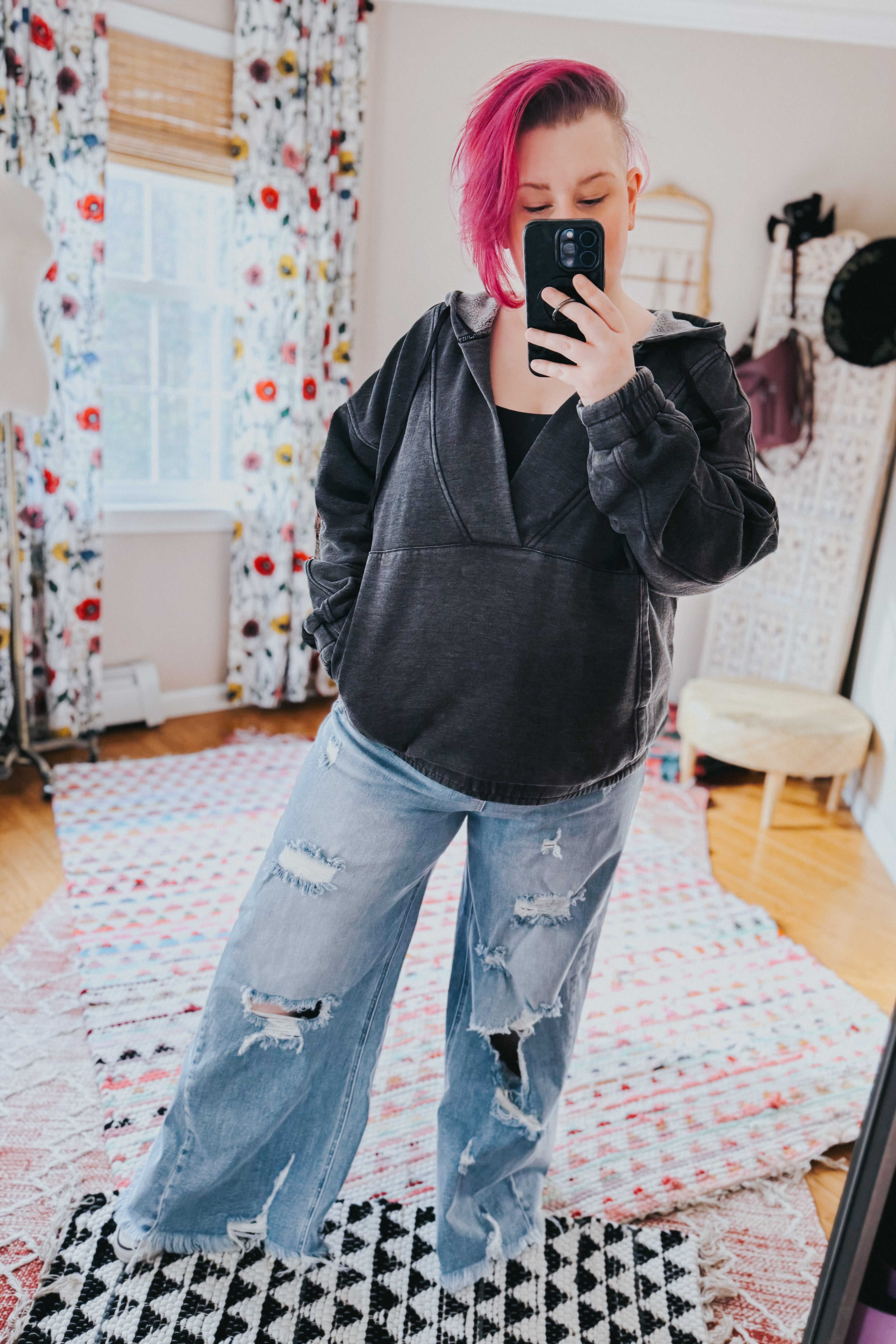 Woman with pink hair taking mirror selfie wearing charcoal acid wash hoodie and ripped wide-leg jeans in cozy room