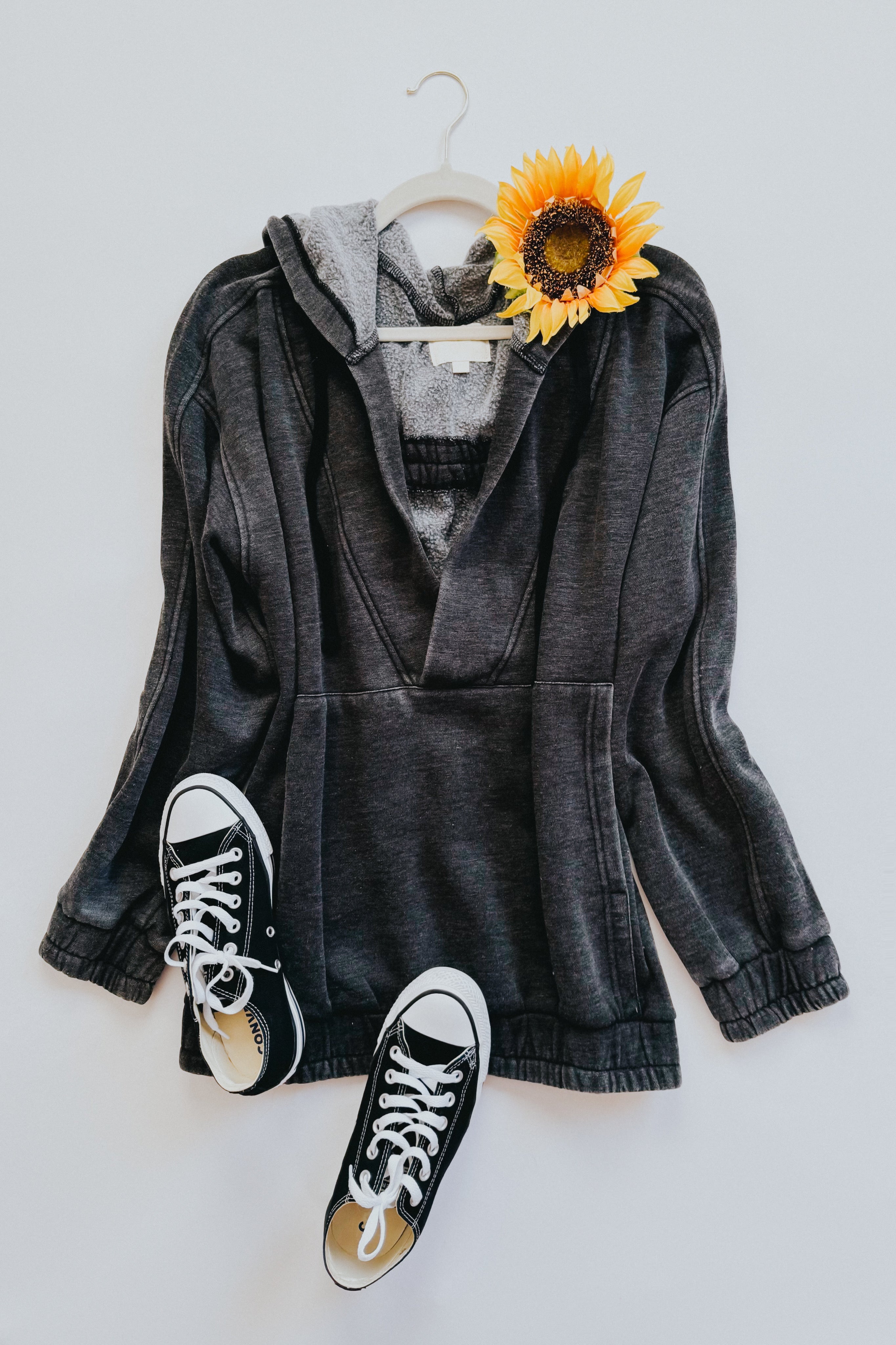 Charcoal acid wash hoodie with front pocket paired with black canvas sneakers and a sunflower accent.