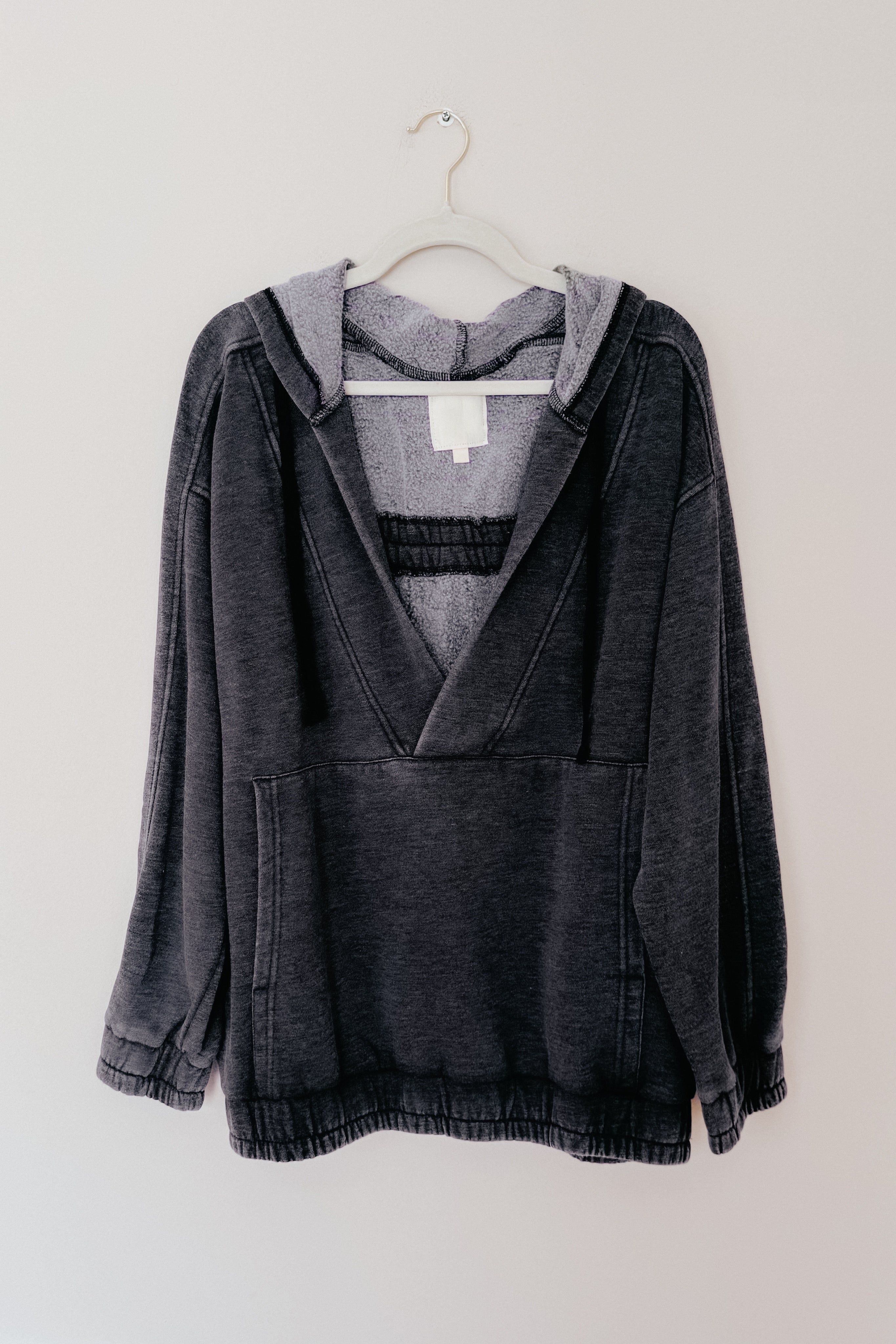 Charcoal acid wash hoodie with relaxed fit and kangaroo pocket hanging on white hanger against plain wall