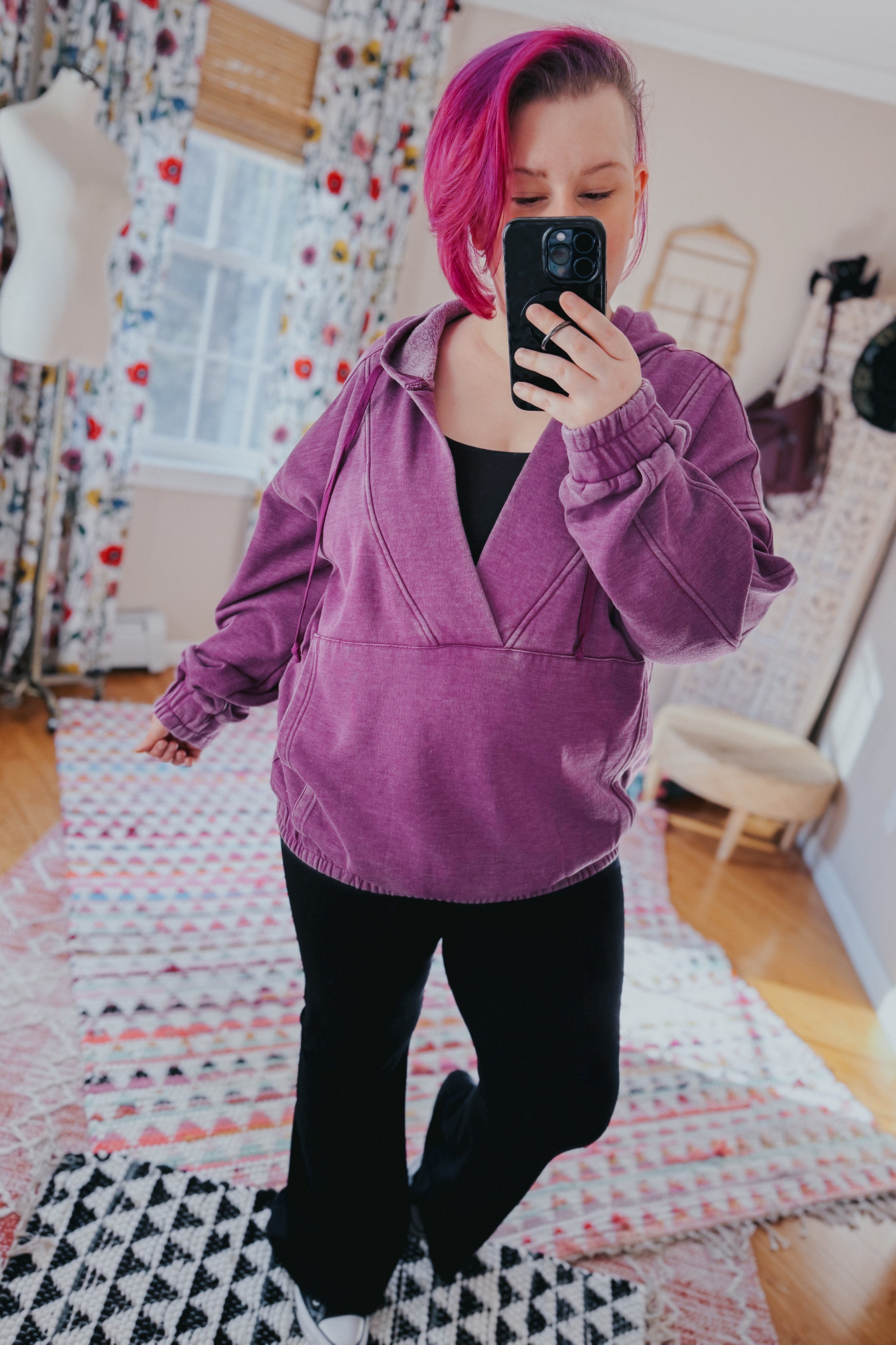 Woman with pink hair wearing plum acid wash hoodie with elastic cuffs and hood taking mirror selfie indoors