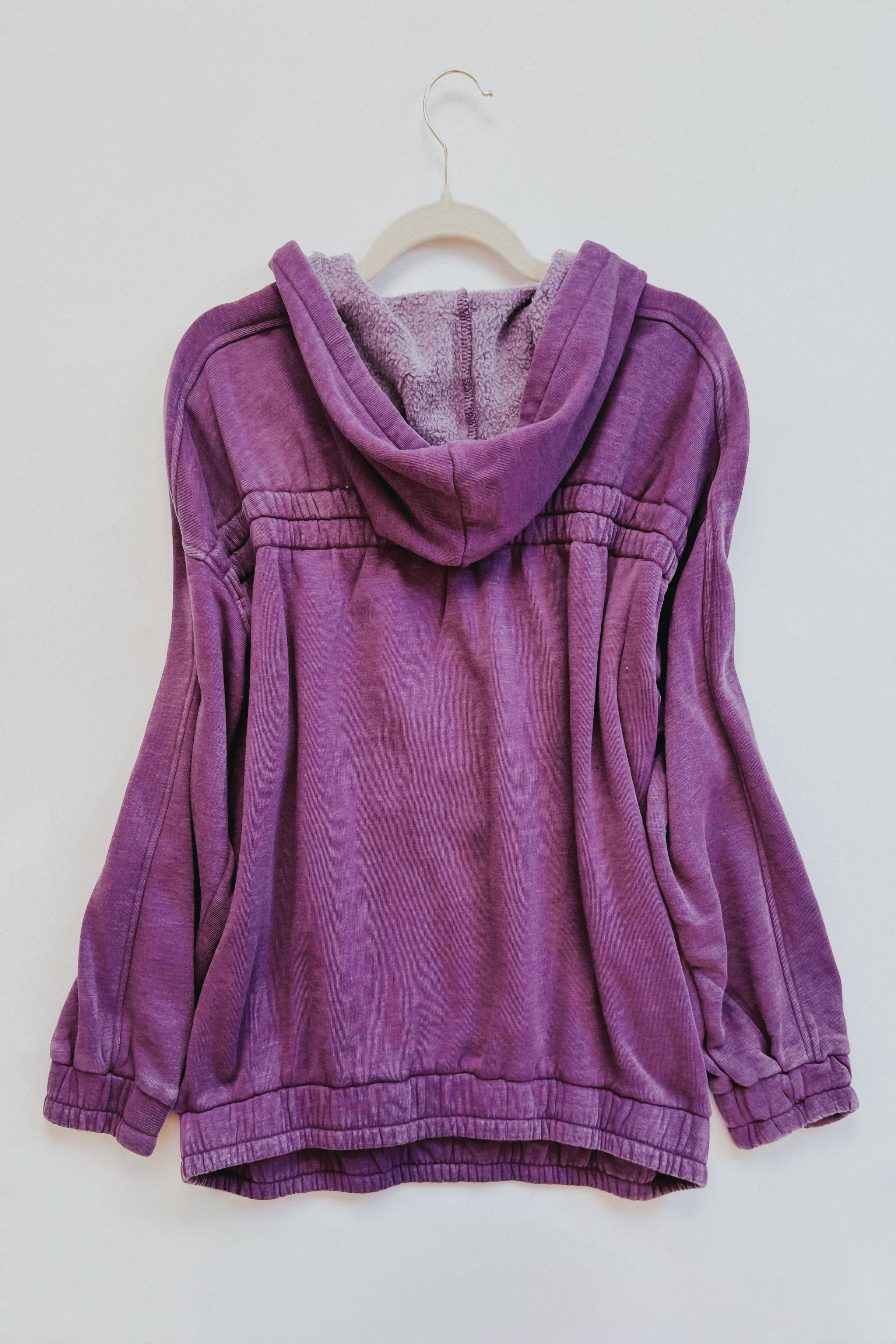 Back view of plum acid wash hoodie with gathered detailing and plush-lined hood hanging on white hanger