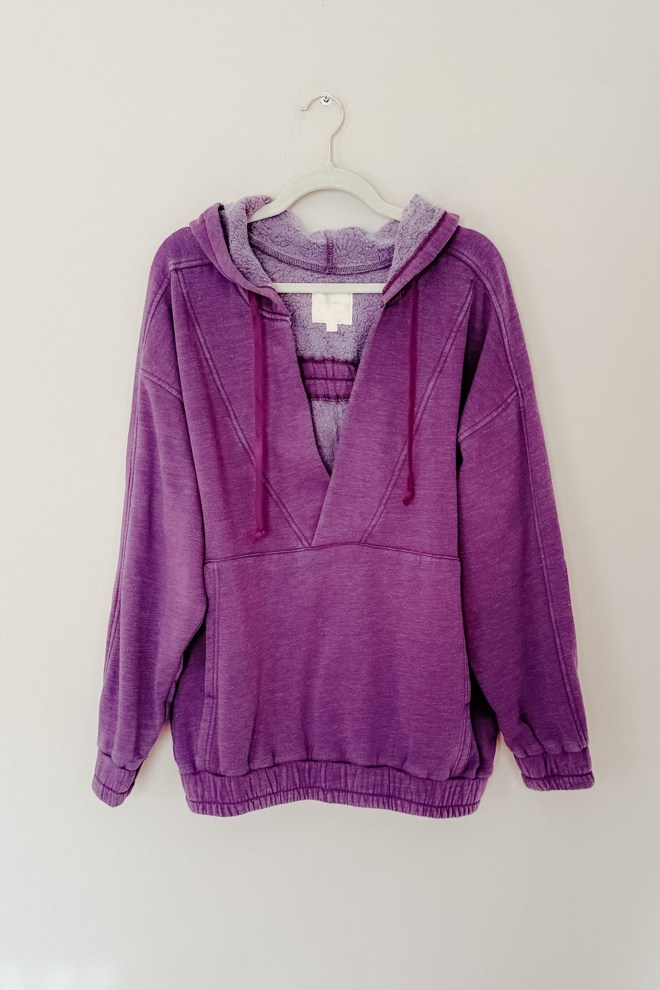 Plum acid wash hoodie with plush-lined hood and drawstrings hanging on white hanger against plain wall
