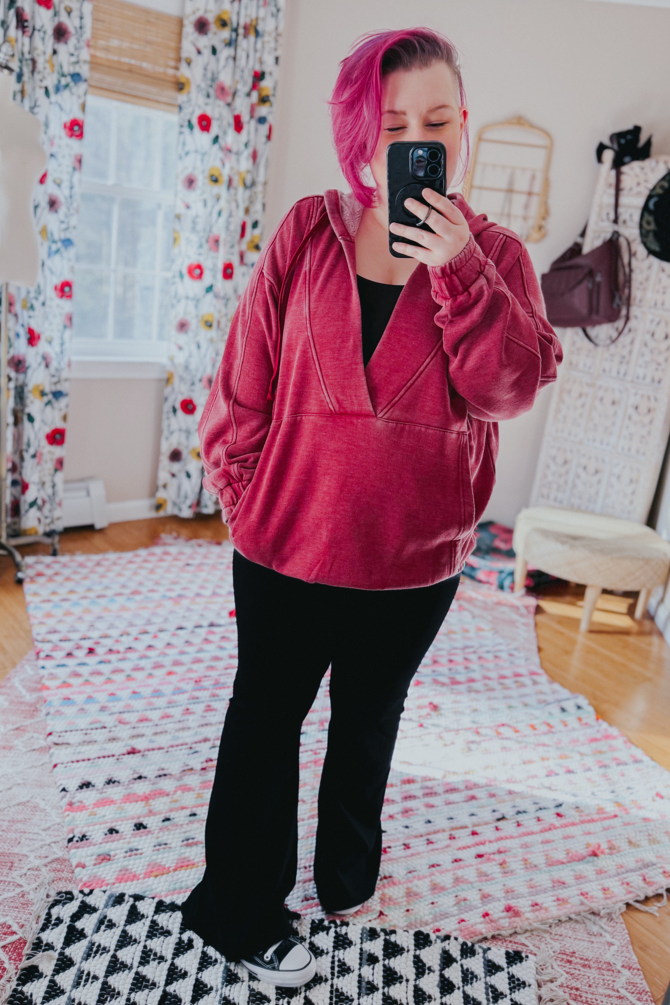 Woman with short magenta hair wearing wine-colored acid wash hoodie with gathered sleeves taking mirror selfie indoors