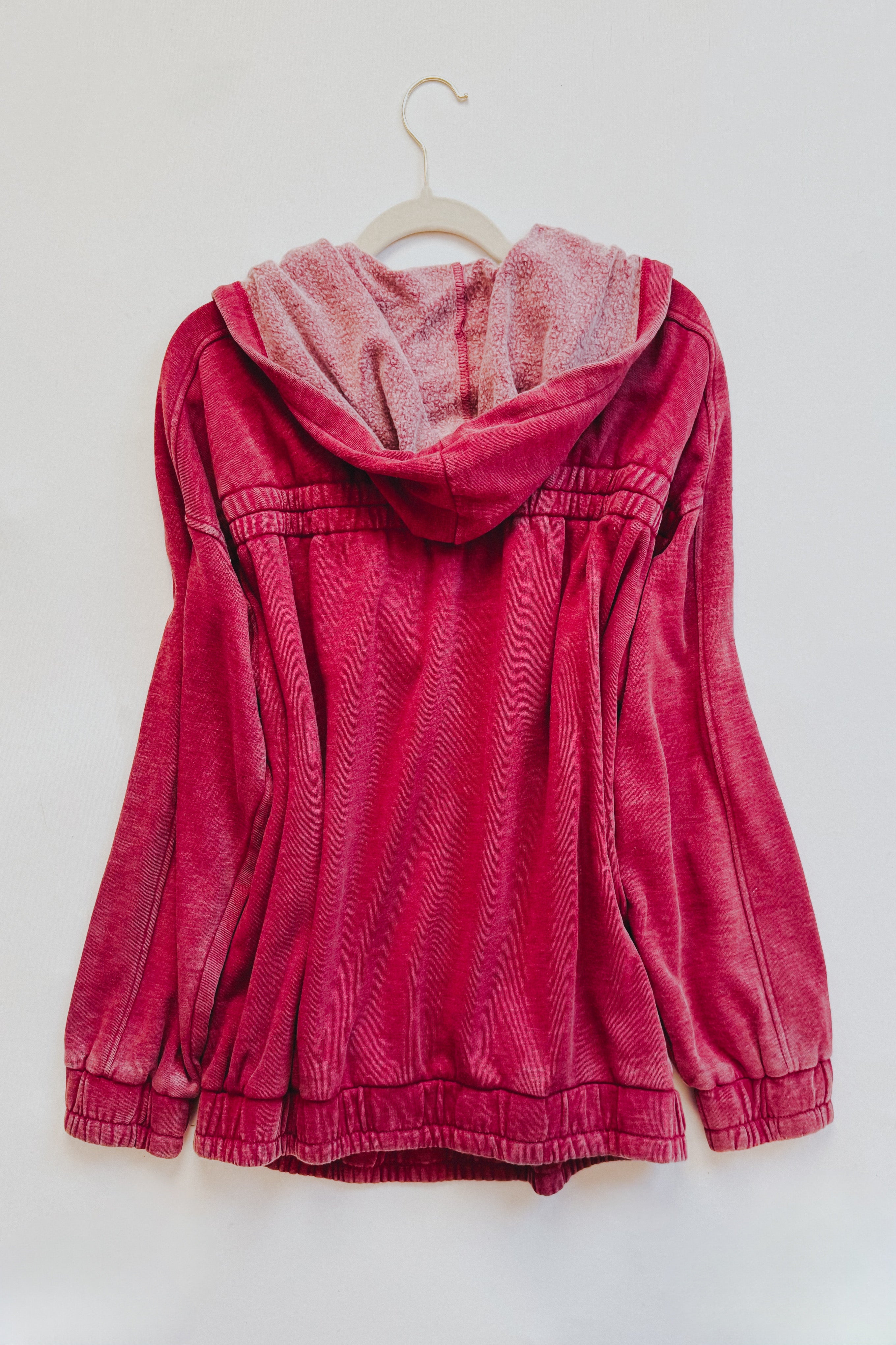 Back view of wine-colored acid wash hoodie with plush-lined hood and gathered waist detail on hanger