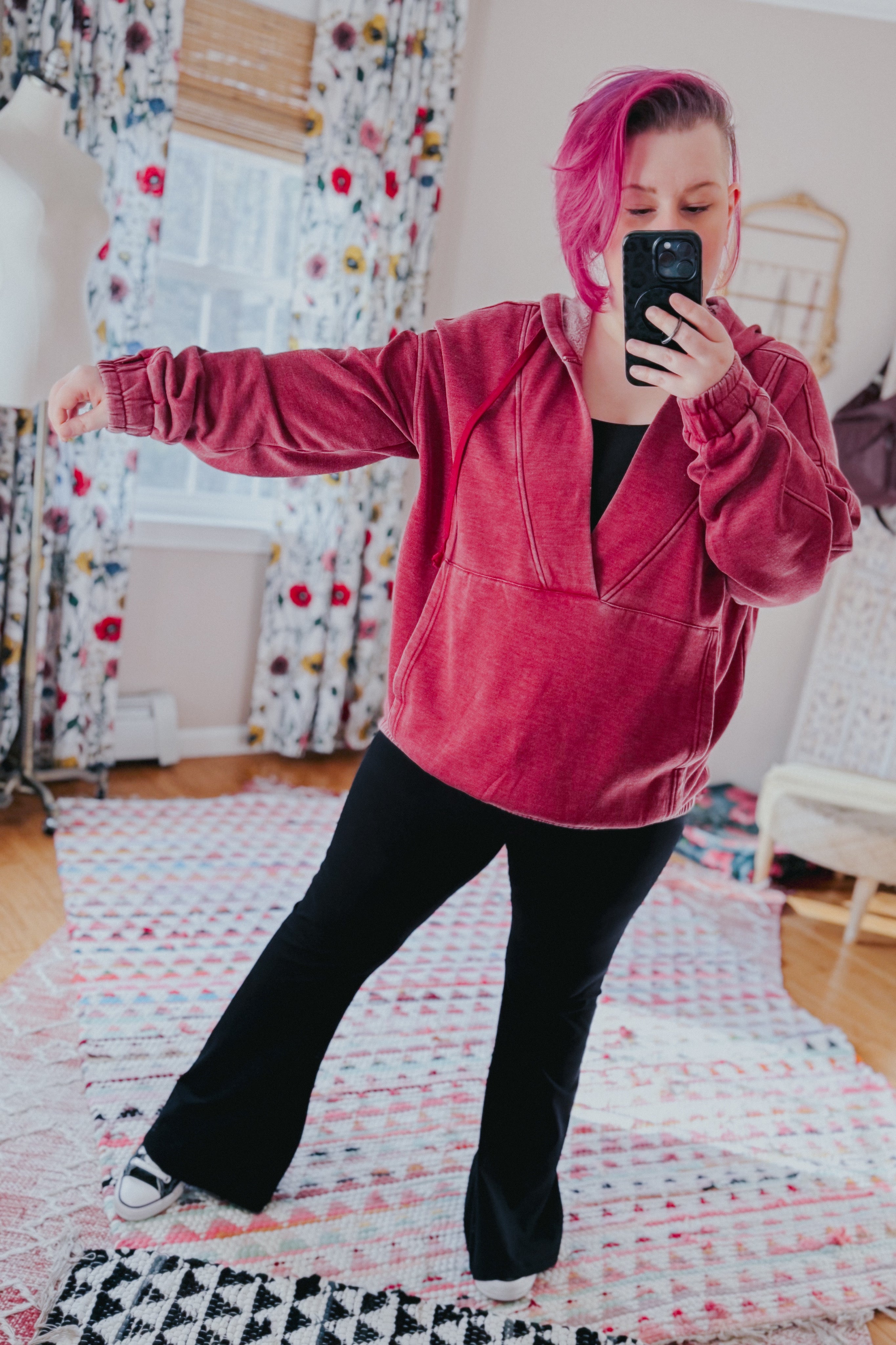 Woman with magenta hair wearing a wine-colored acid wash hoodie with elastic cuffs taking mirror selfie indoors