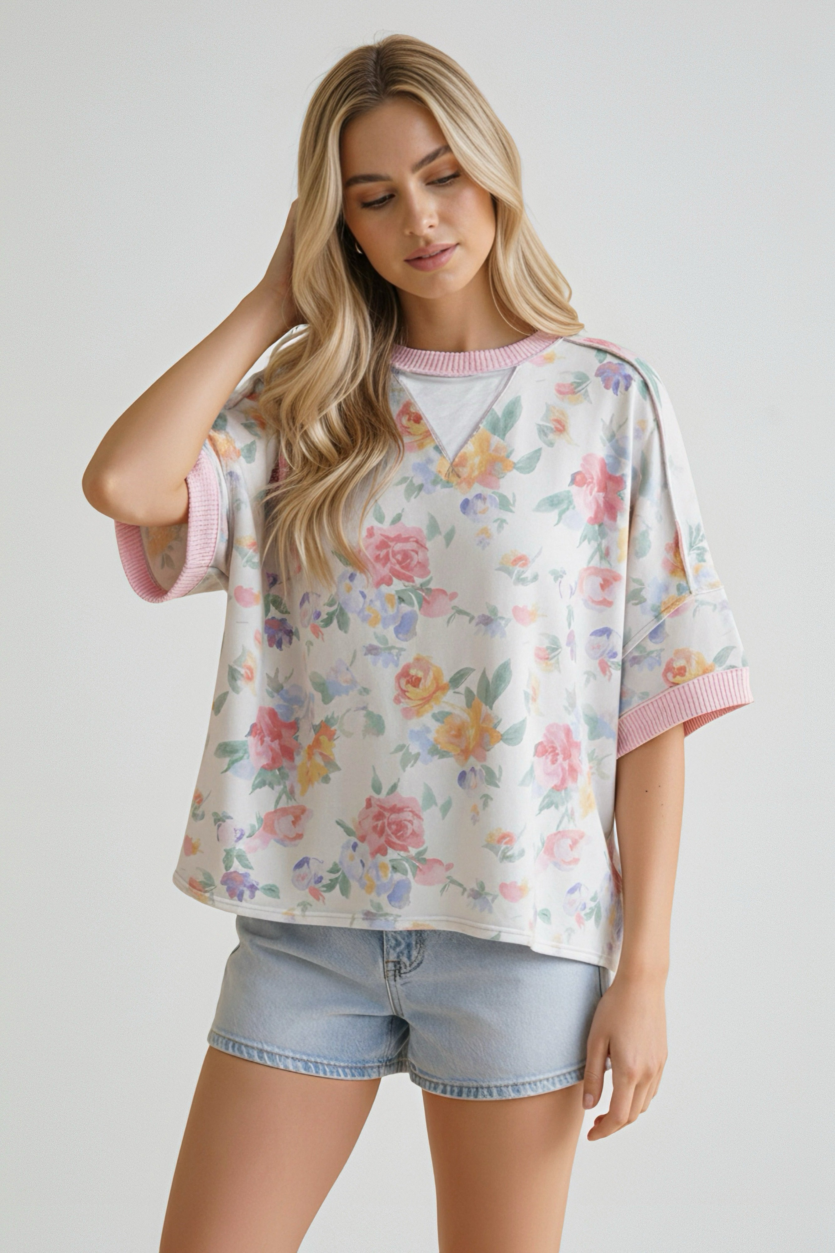 Woman wearing a relaxed fit floral top with pink ribbed collar and cuffs paired with light denim shorts