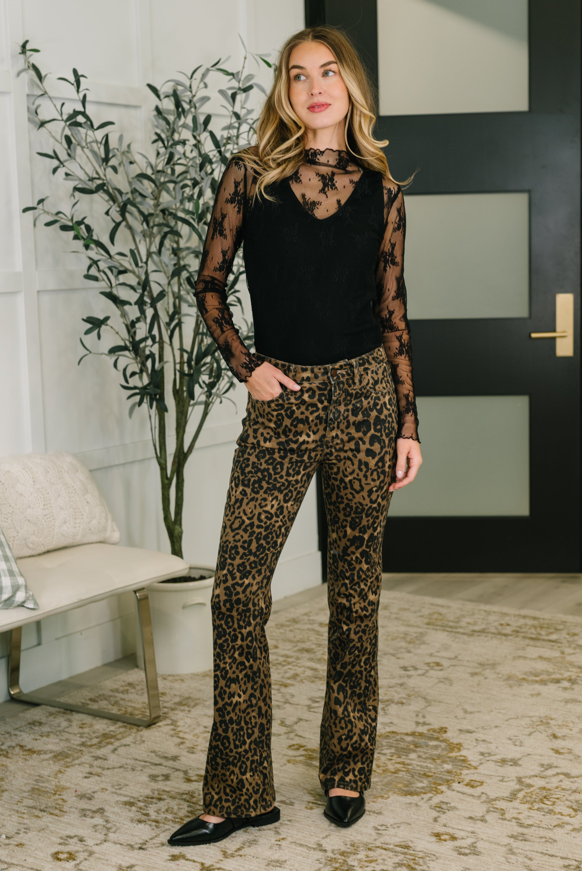 Woman wearing brown leopard print high waist bootcut jeans paired with a sheer black floral long-sleeve top indoors