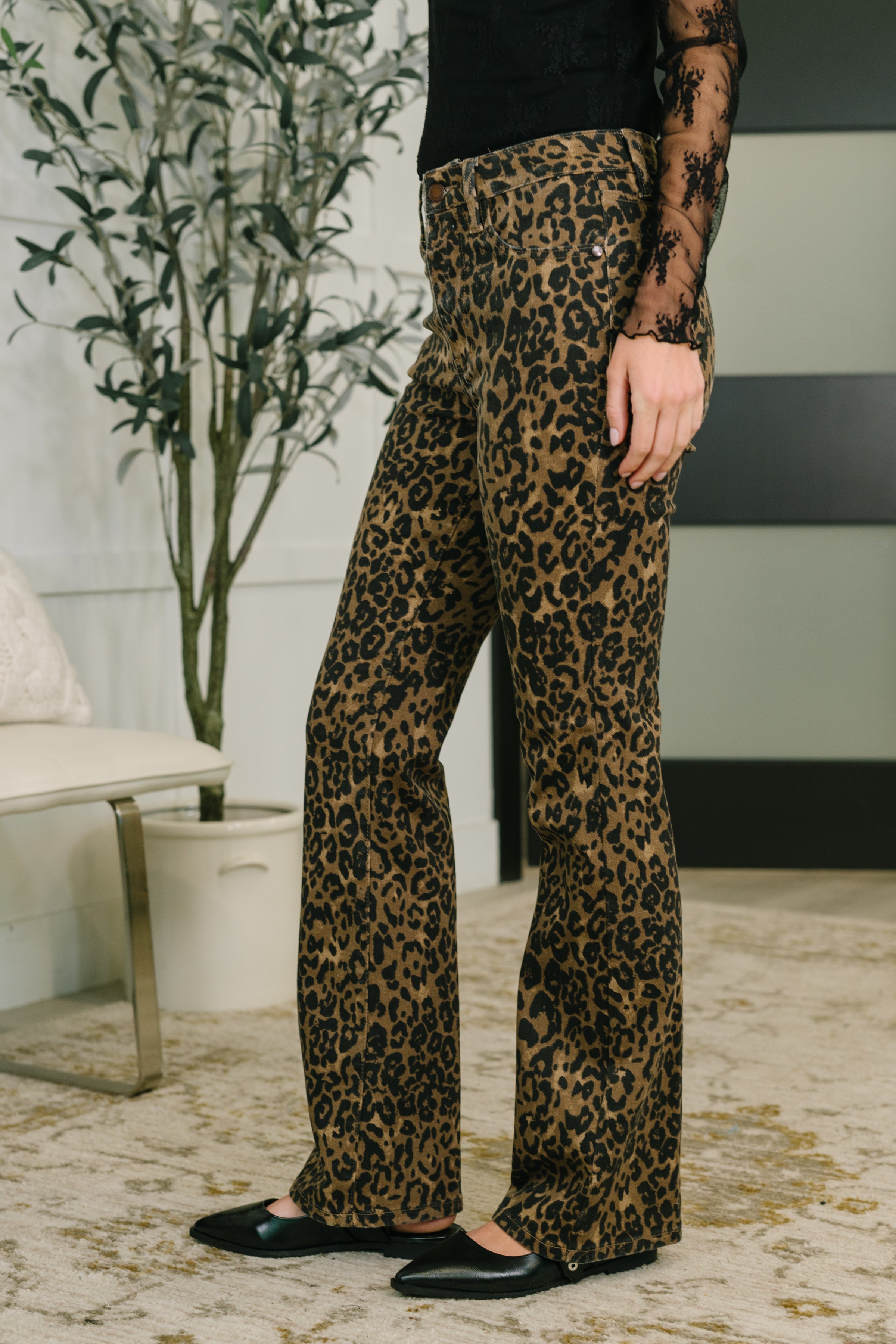 Woman wearing brown leopard print high waist bootcut jeans paired with black lace top and flats indoors