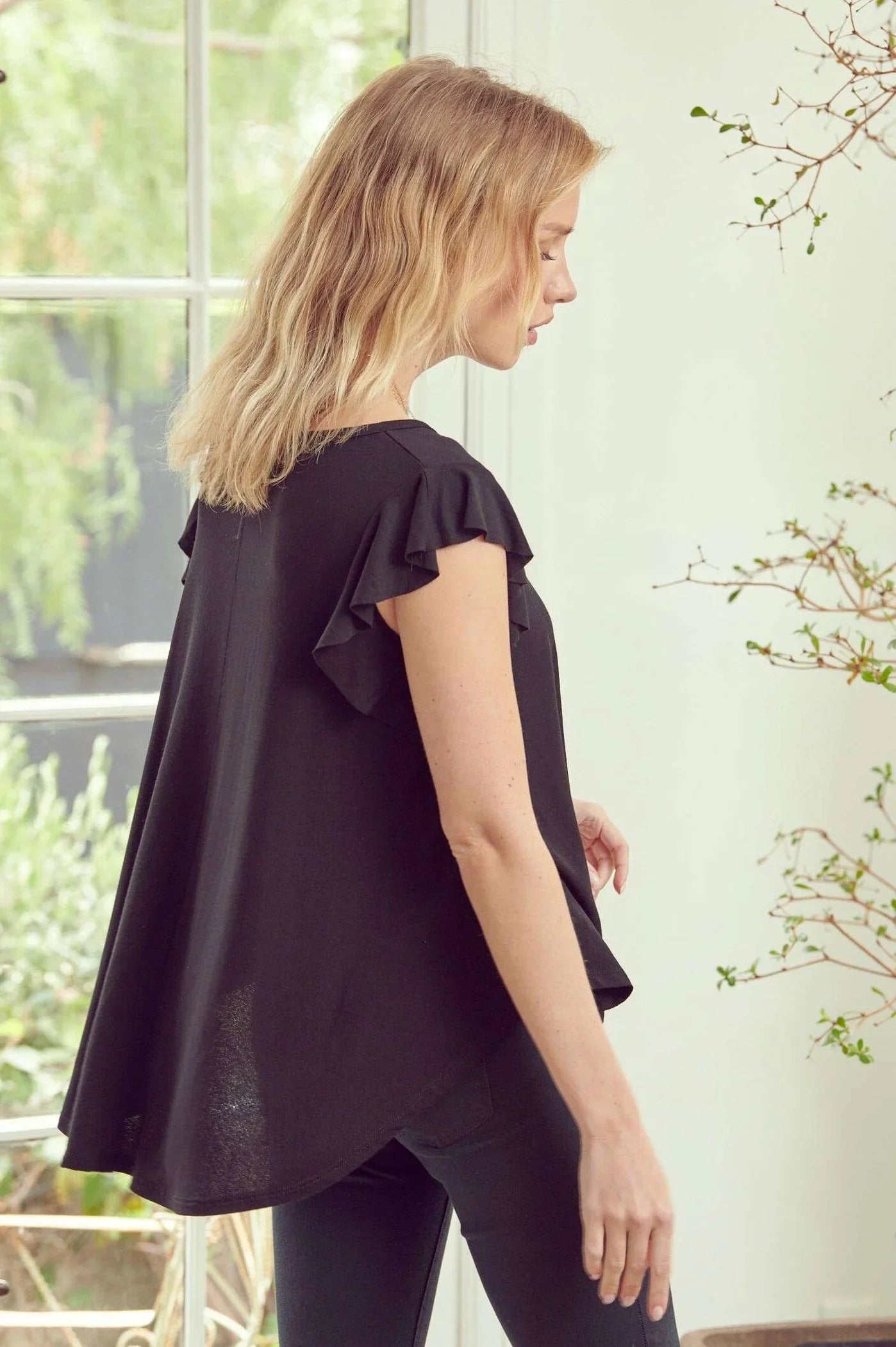 Woman wearing black ruffle sleeve top with flowy silhouette standing indoors near window with natural light