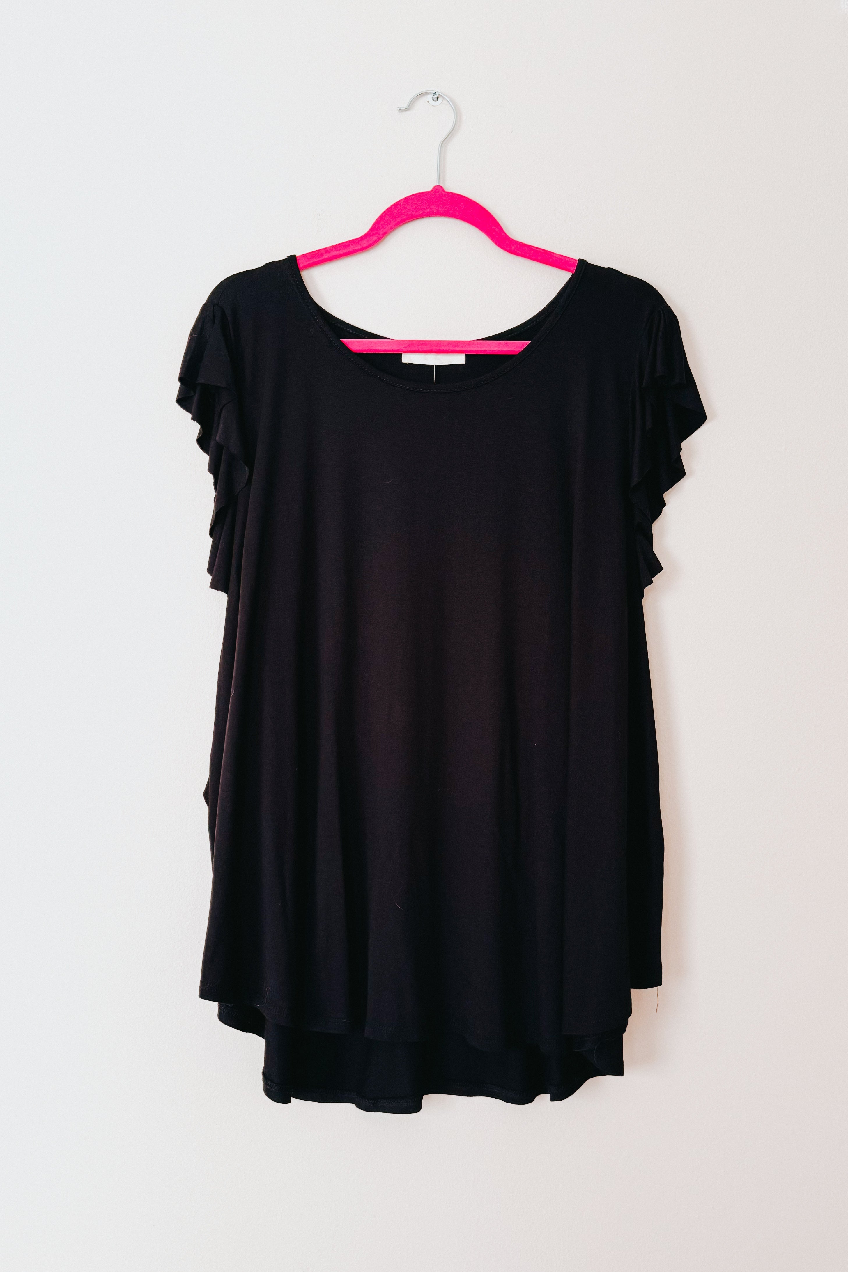 Black top with layered ruffle sleeves hanging on bright pink hanger against plain white background