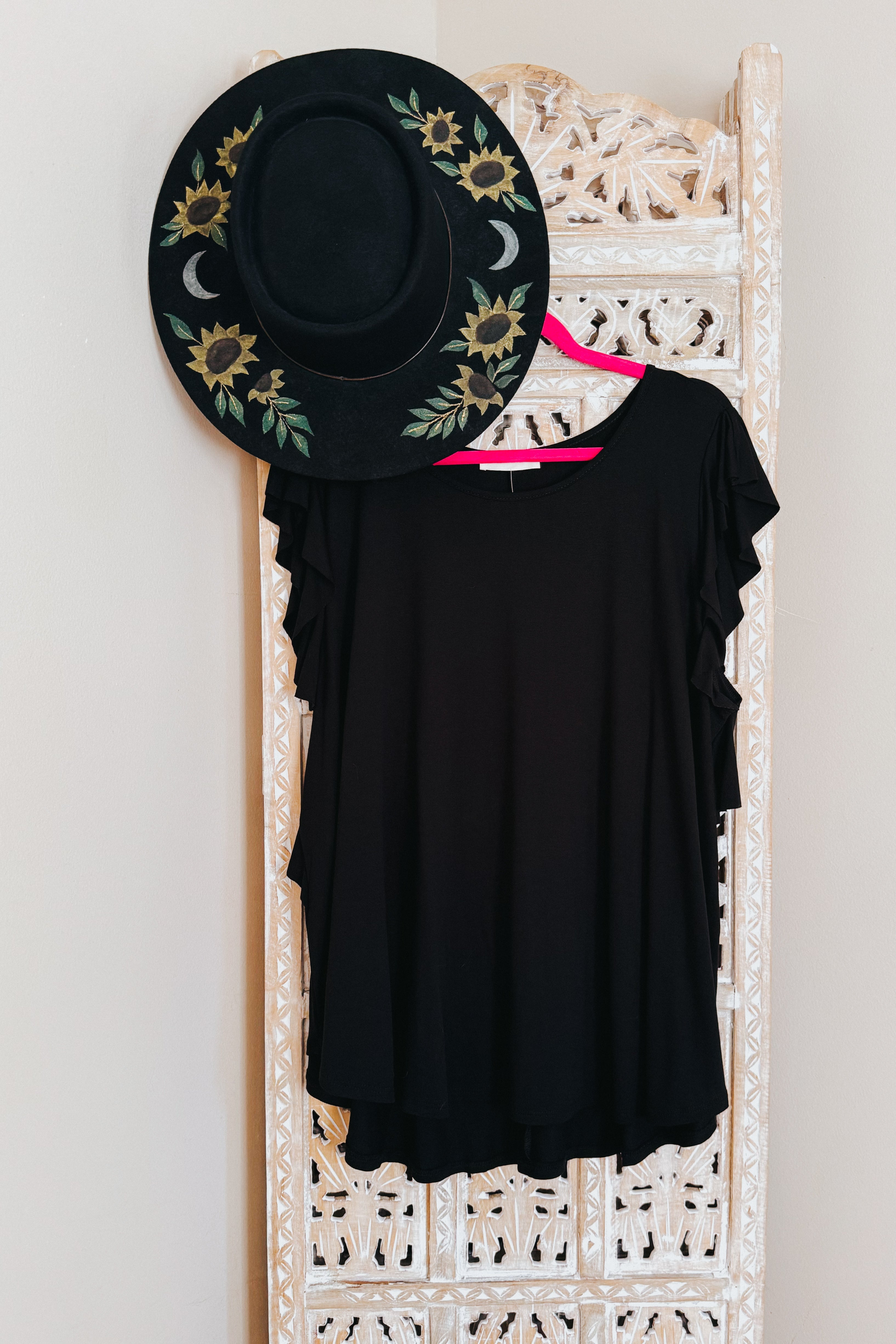 Black ruffle sleeve top paired with black wide-brim hat featuring sunflower and moon embroidery on carved screen