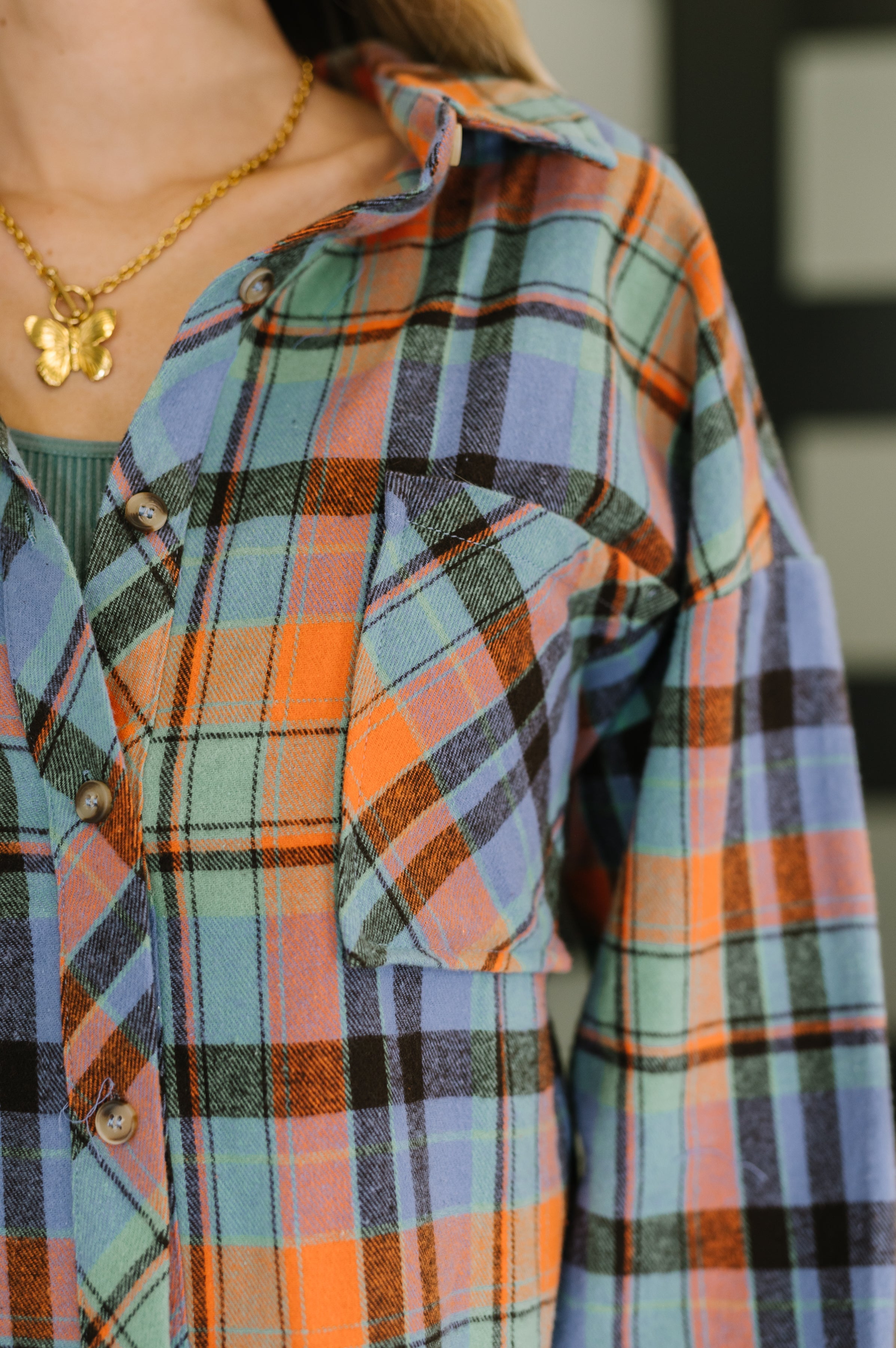 Close-up of blue and orange plaid button-down shirt with pocket and gold butterfly necklace on model
