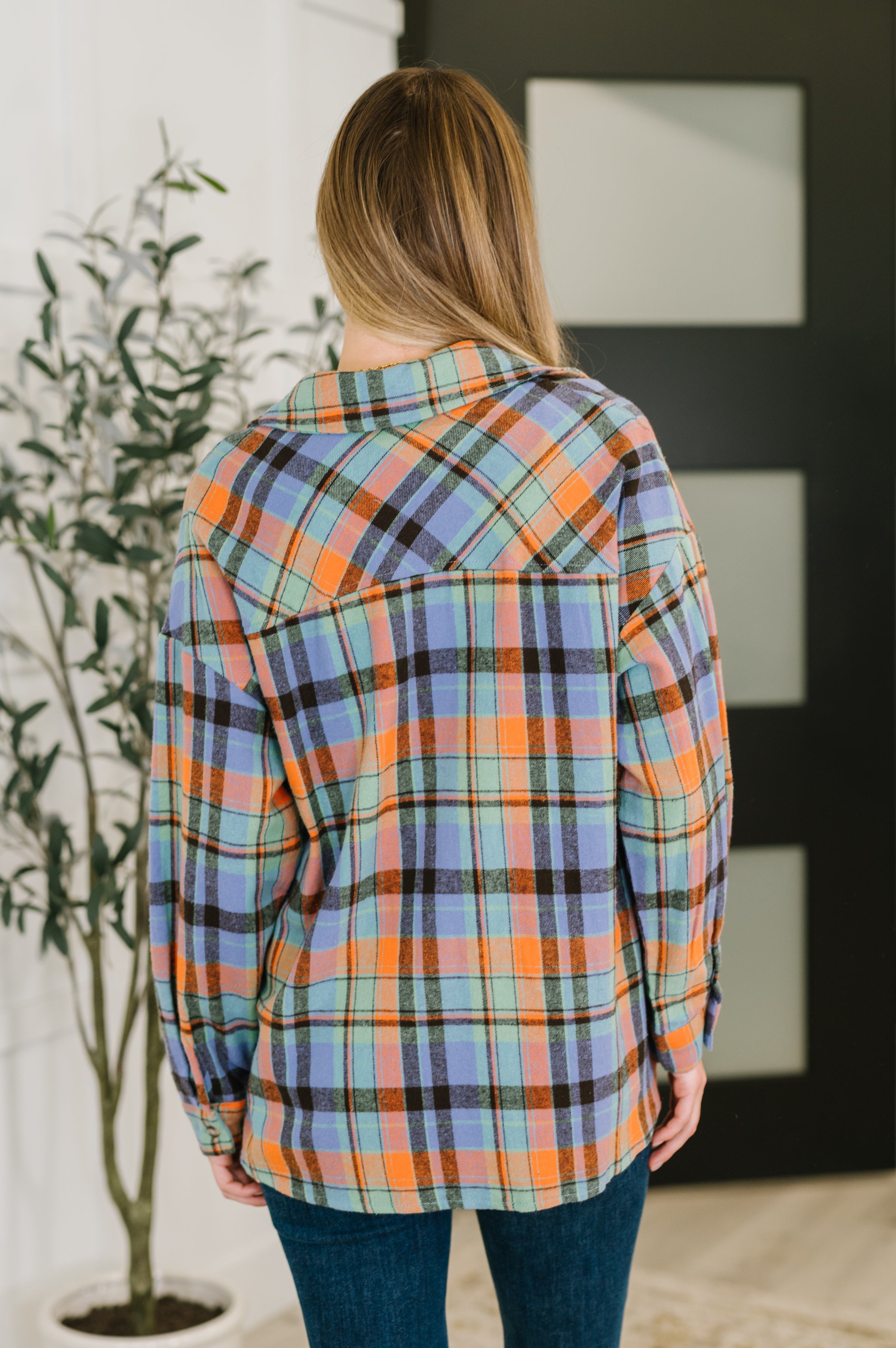 Woman from behind wearing blue and orange plaid shirt with relaxed fit paired with dark blue jeans indoors