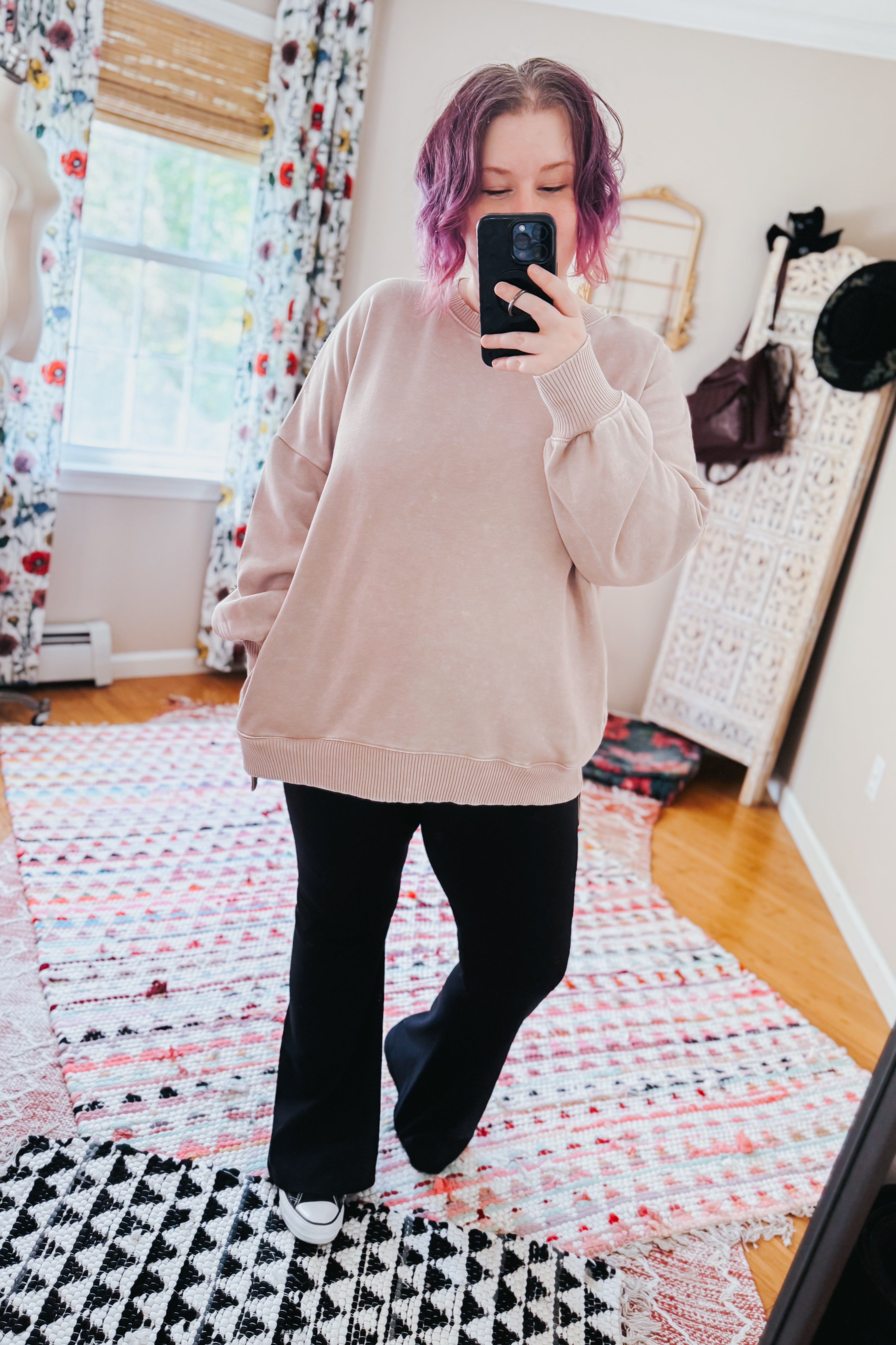 Woman with purple hair taking mirror selfie wearing ash mocha pullover and black flared pants indoors on patterned rugs