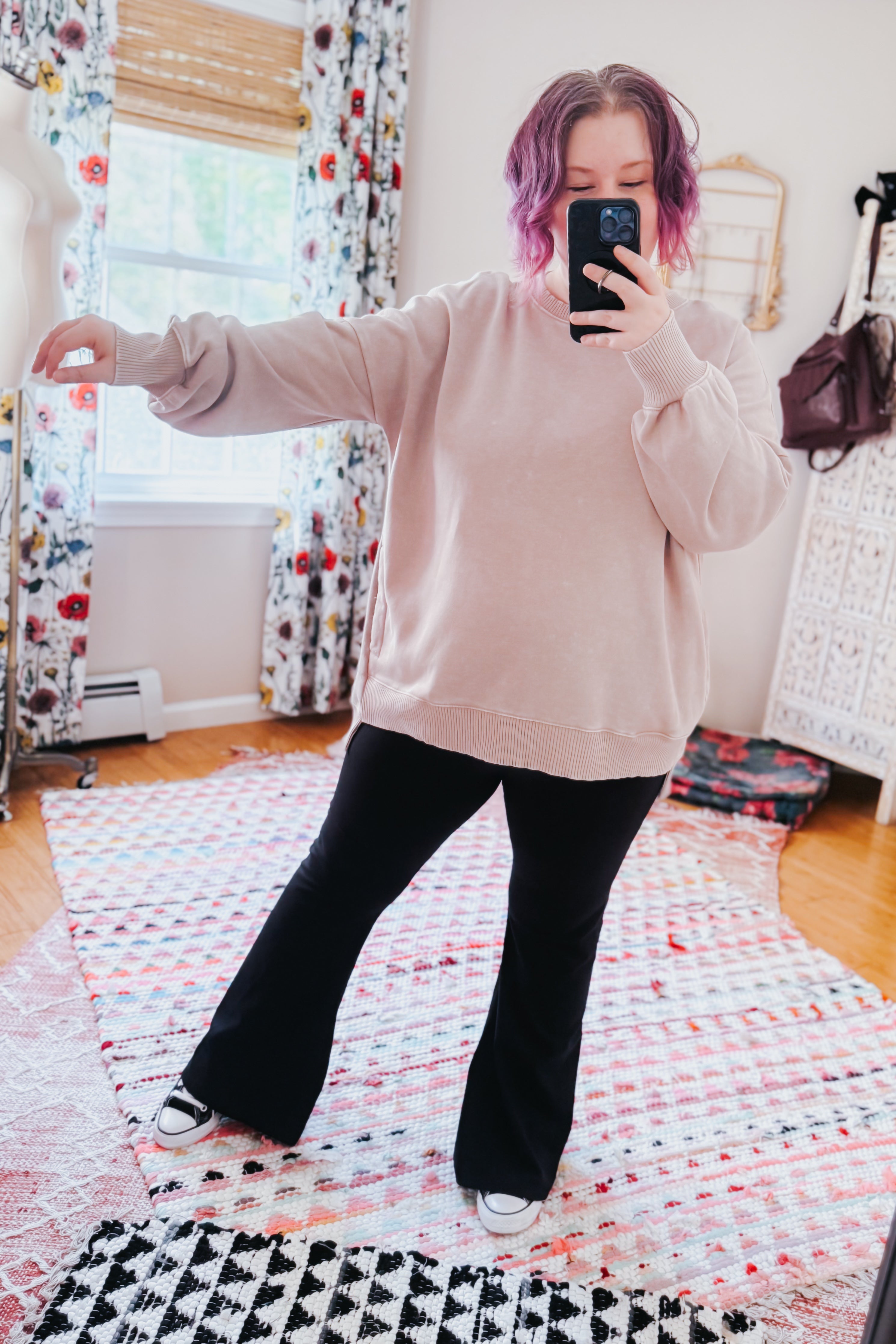 Woman with purple hair wearing ash mocha mineral wash pullover and black flared pants taking mirror selfie indoors