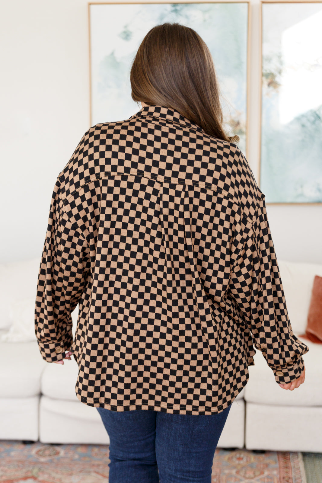 Woman wearing oversized brown checkered shacket with relaxed fit standing indoors facing away from camera