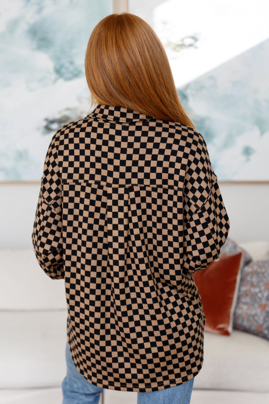 Woman wearing brown and black checkered shacket with relaxed fit standing indoors with back facing camera