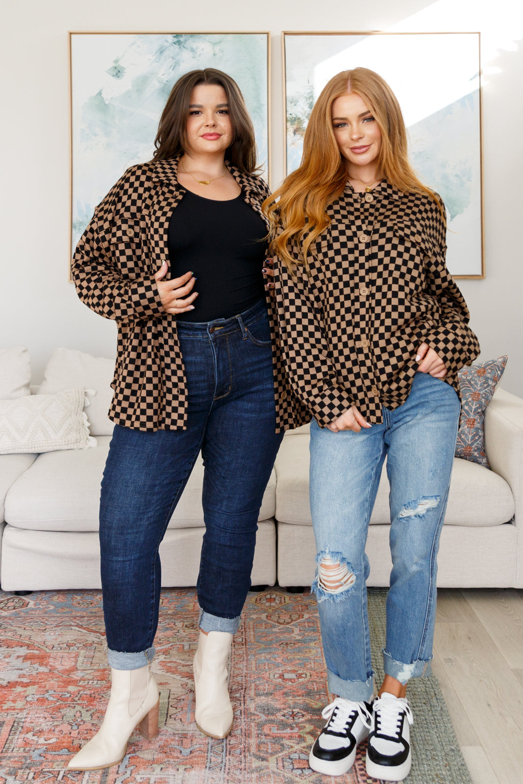 Two women wearing brown checkered shackets styled with casual denim and standing indoors on a patterned rug