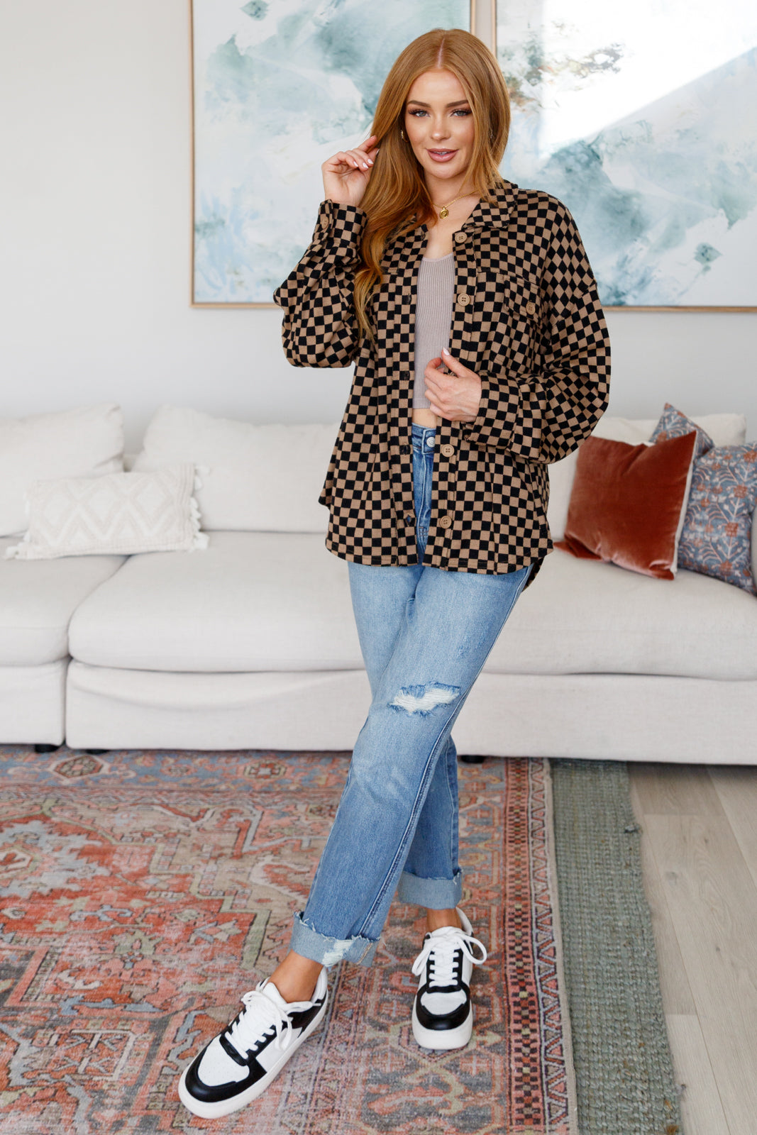 Woman wearing brown checkered oversized shacket paired with light washed ripped jeans and black and white sneakers indoors