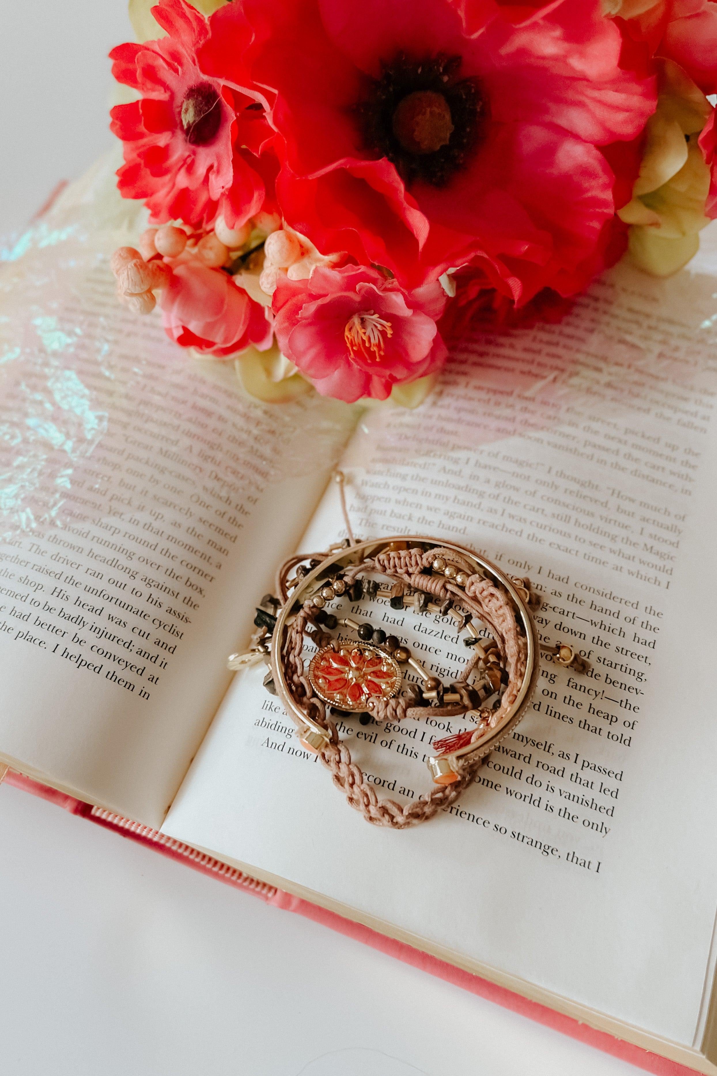 Beige stackable bracelet set arranged on an open book with red and pink flowers nearby in soft light