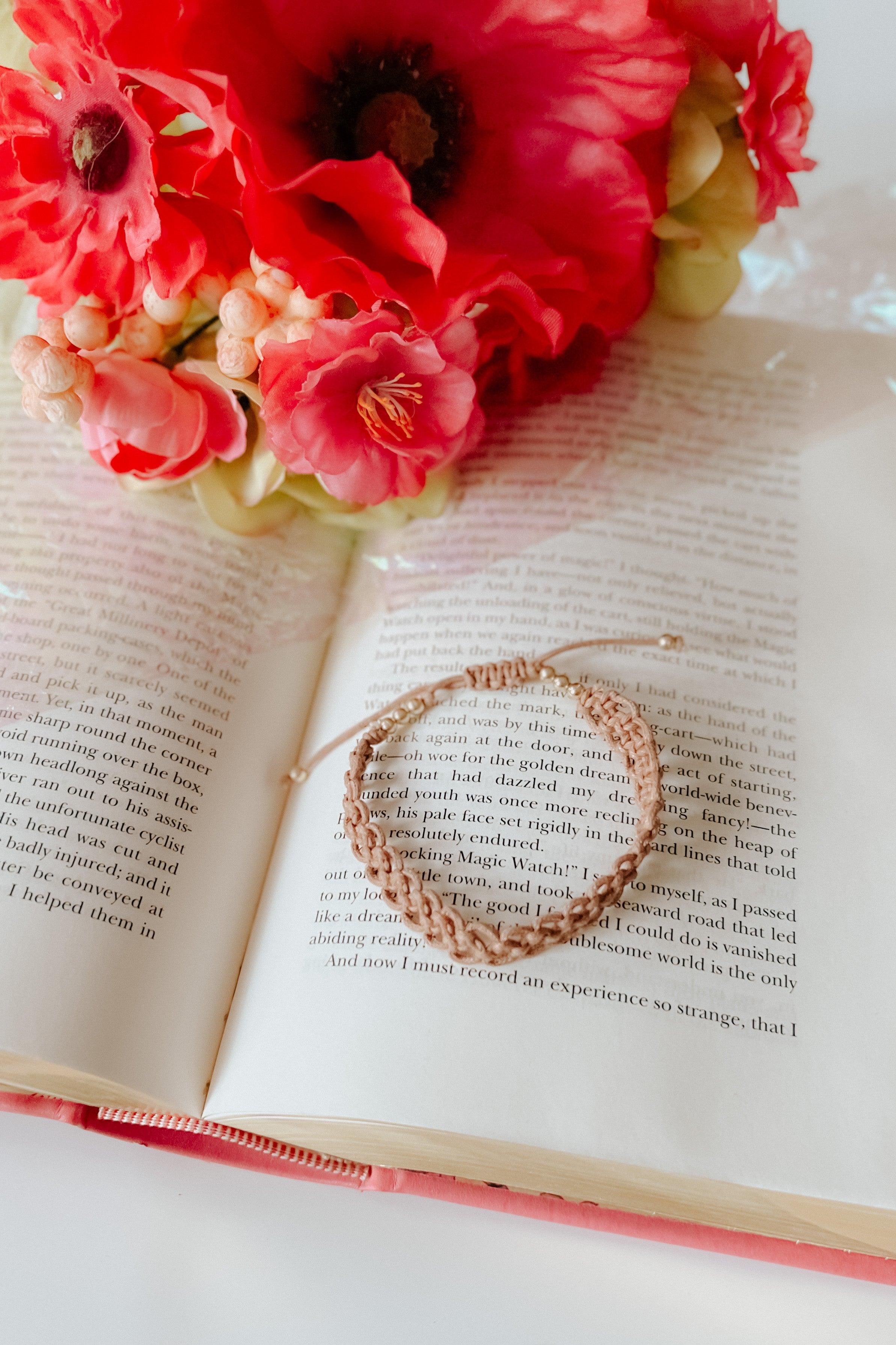 Beige stackable bracelet set resting on an open book beside a cluster of red and pink flowers
