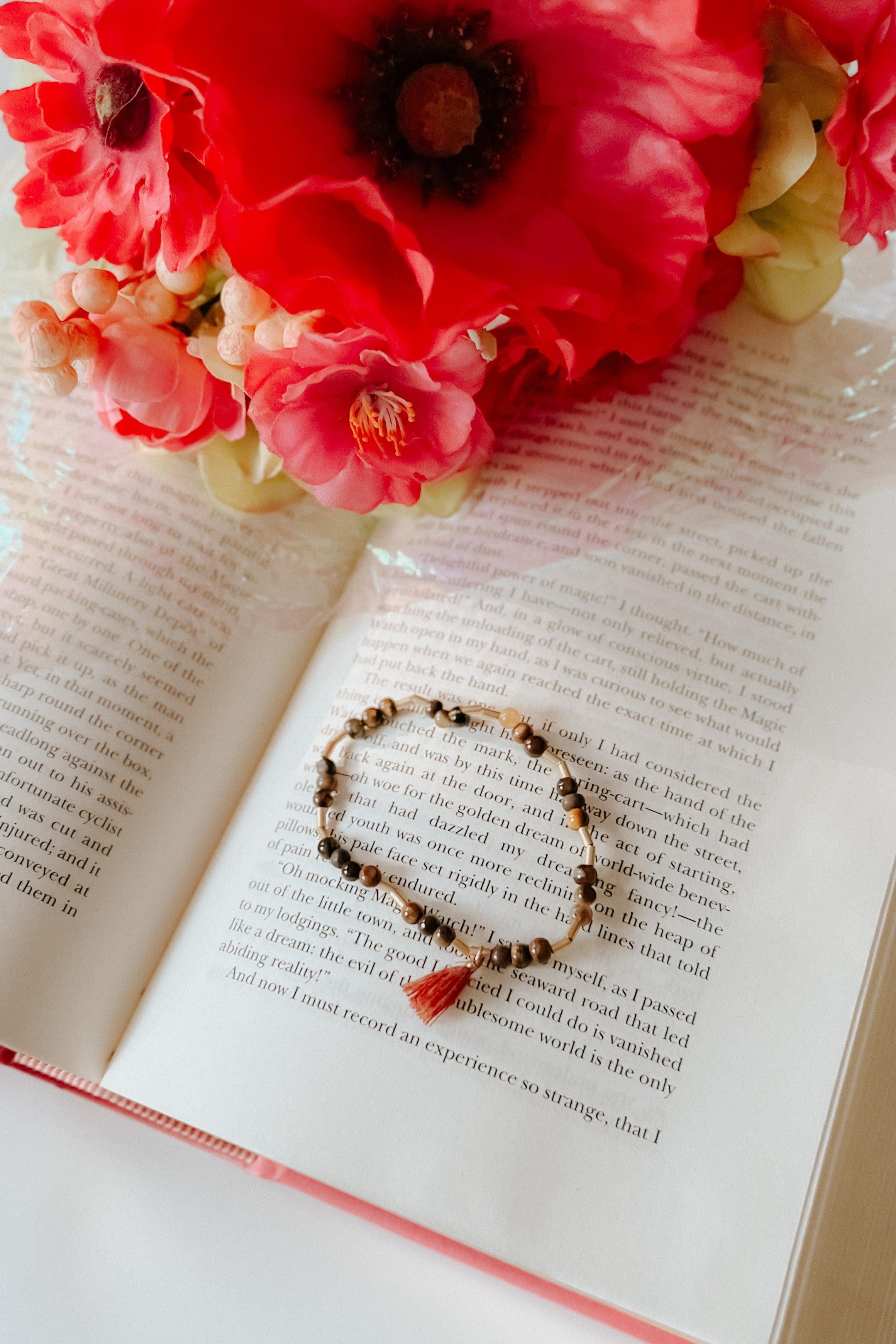 Beige beaded bracelet with tassel detail resting on open book pages with soft natural lighting