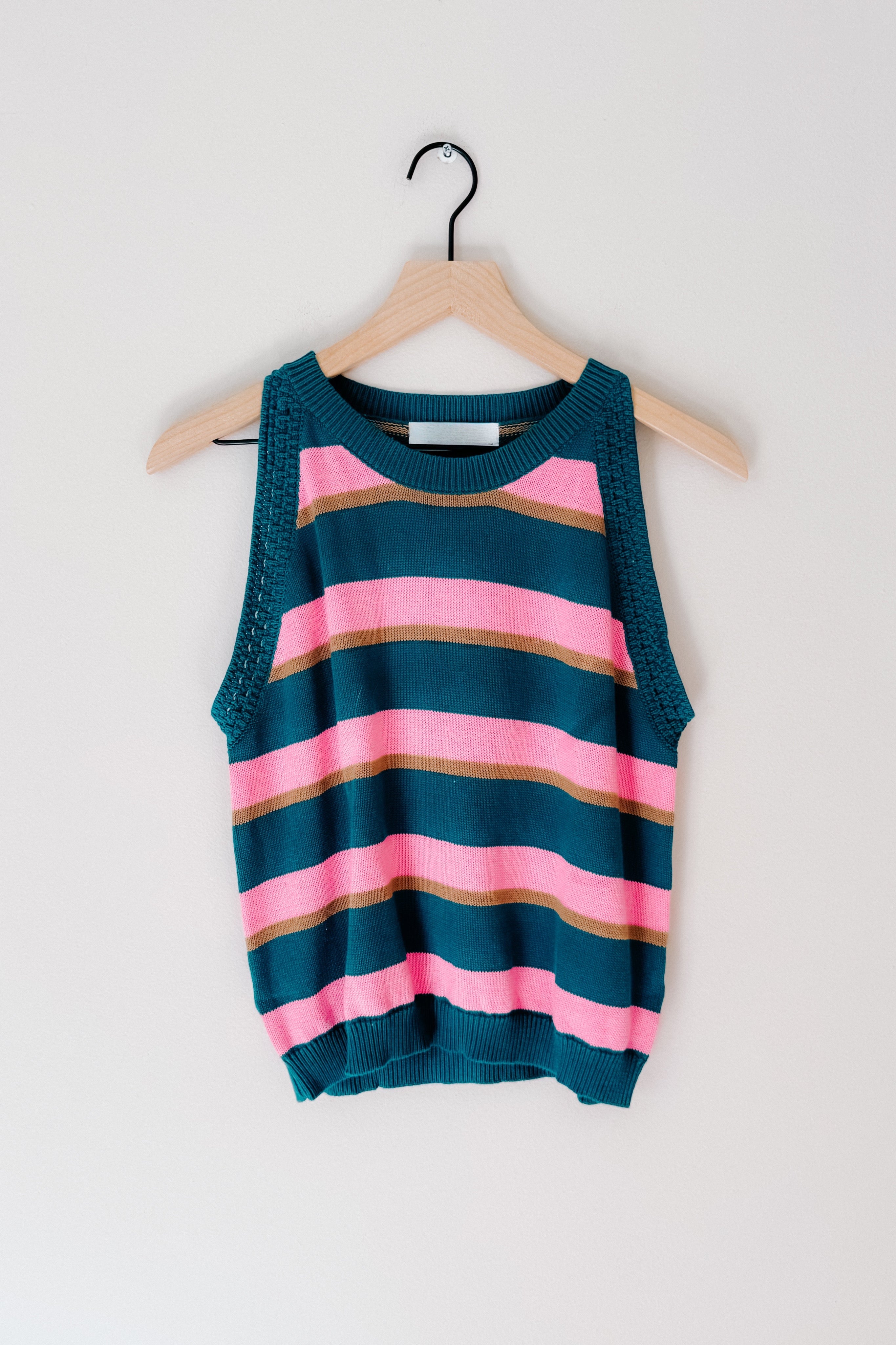 Blue knit sleeveless top with pink and brown horizontal stripes hanging on wooden hanger against white background