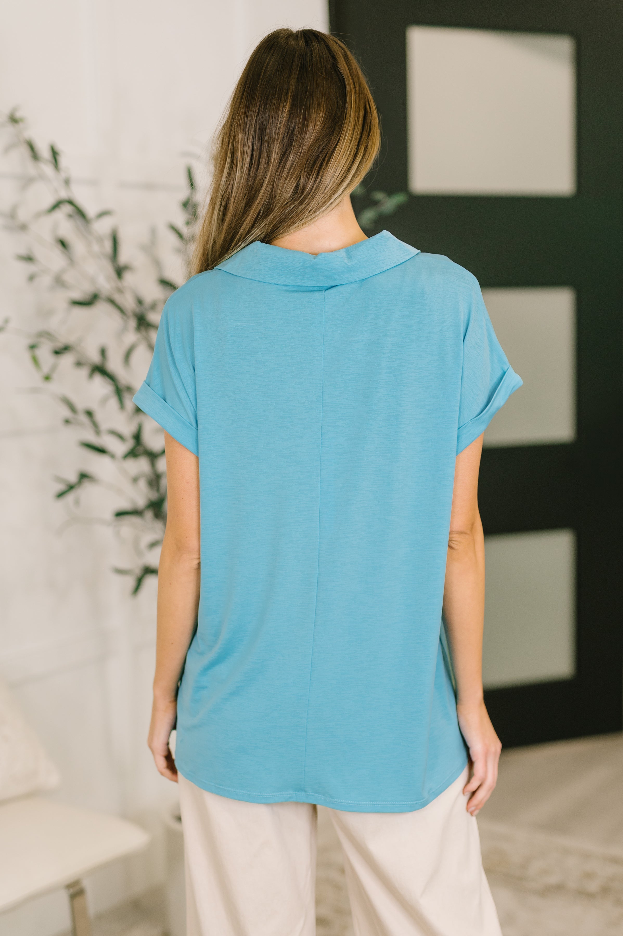 Back view of woman wearing coastal blue short sleeve top with relaxed fit and rolled cuffs indoors