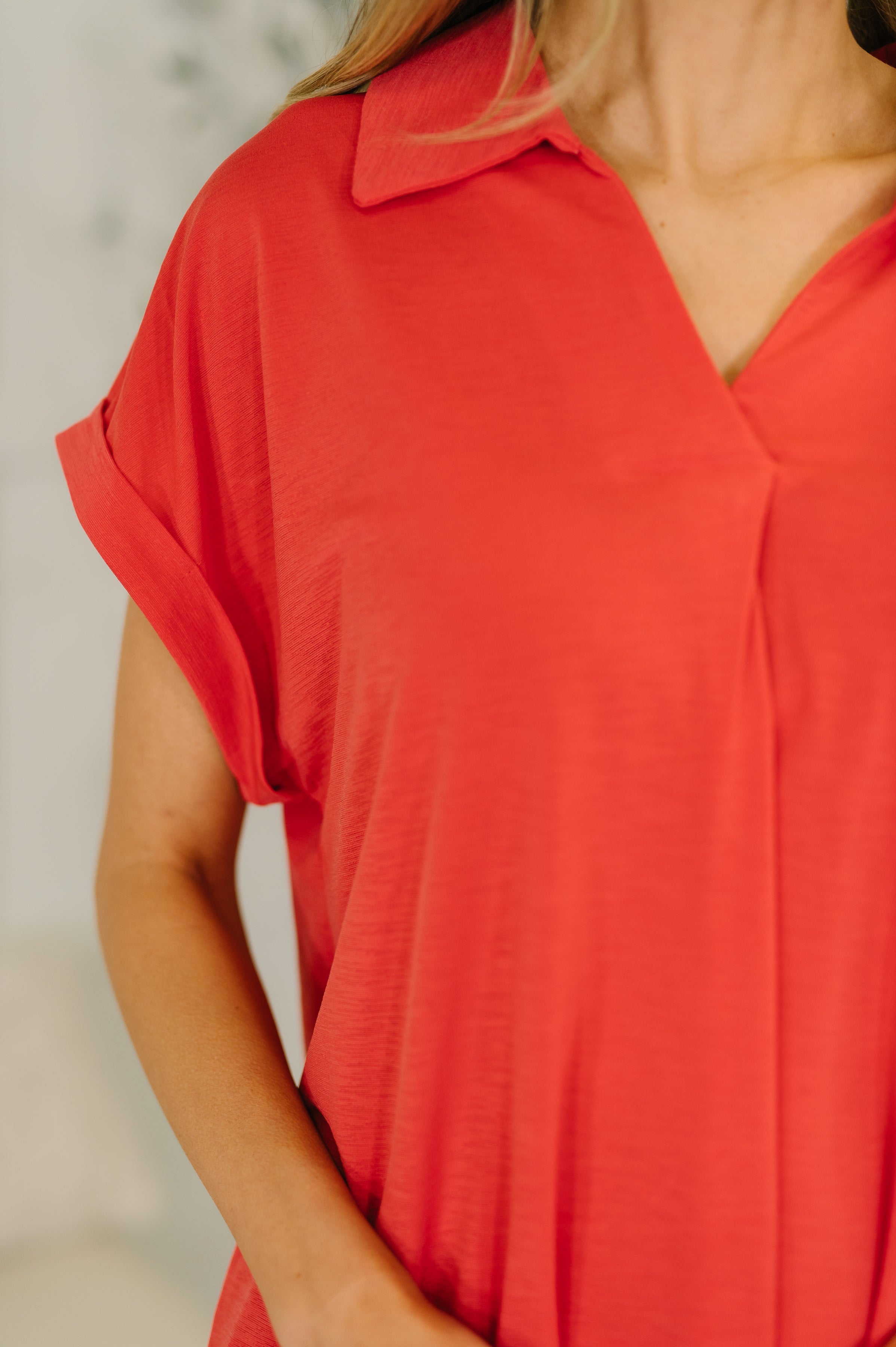 Close-up of woman wearing coral short-sleeve collared top with V-neckline and rolled cuff detail in soft fabric