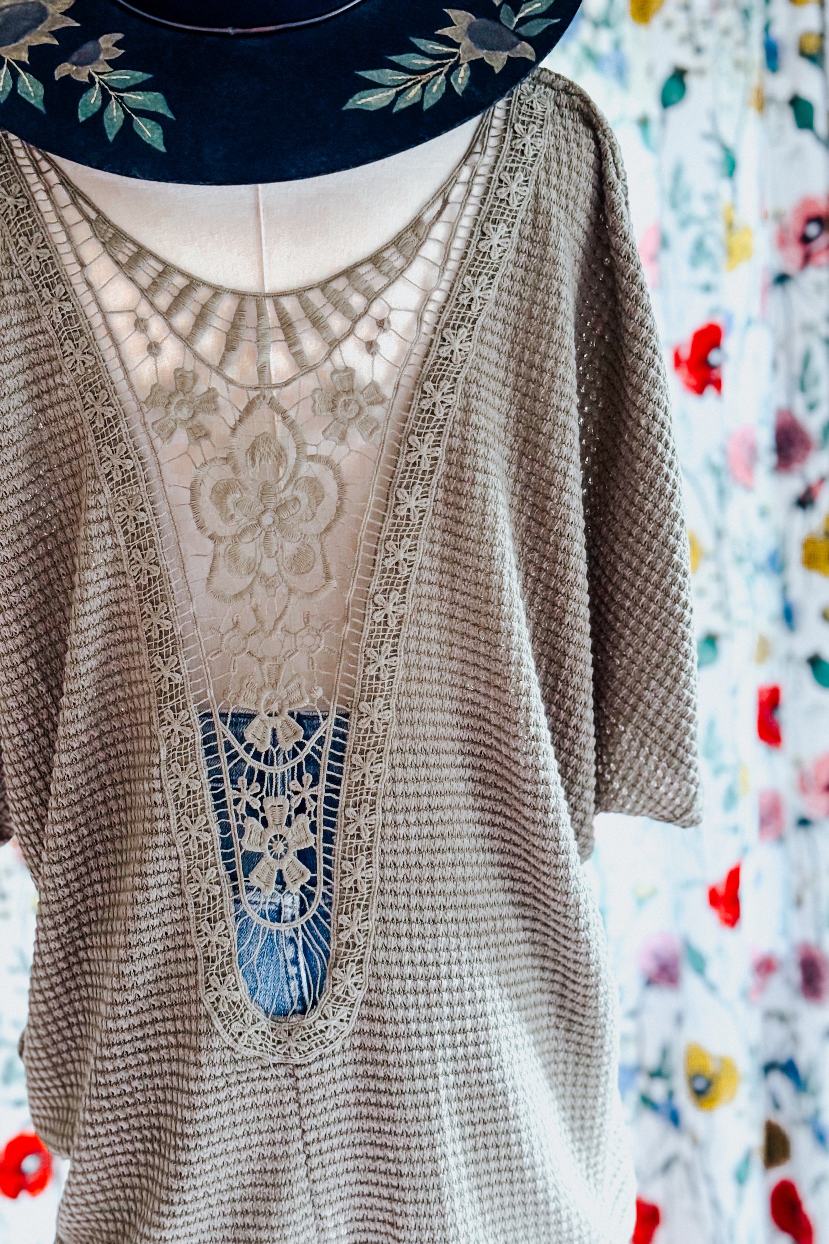Olive toned top featuring intricate lace detail on back with floral embroidery styled on mannequin with hat
