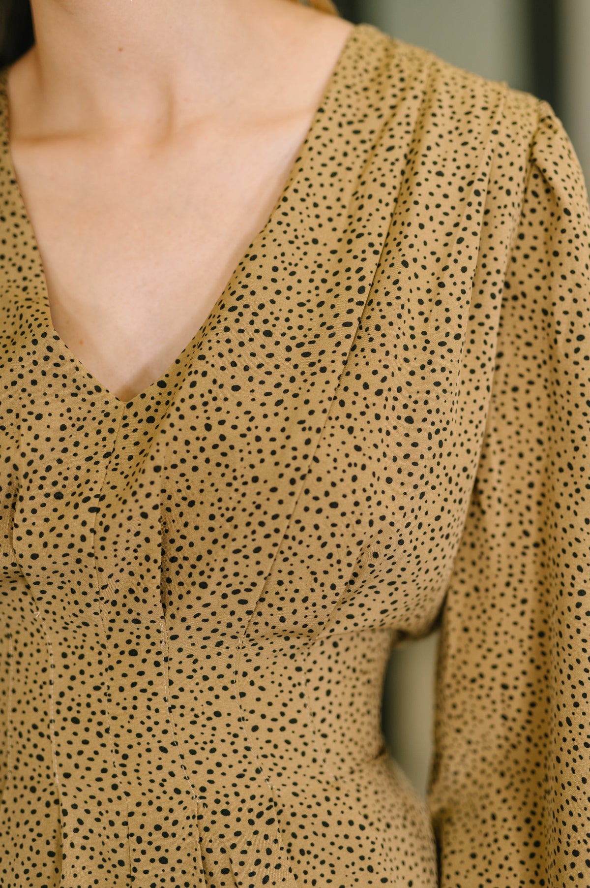 Close-up of a Camel V-neck dress with a black dotted pattern, gathered shoulders, pleated details, and long balloon sleeves