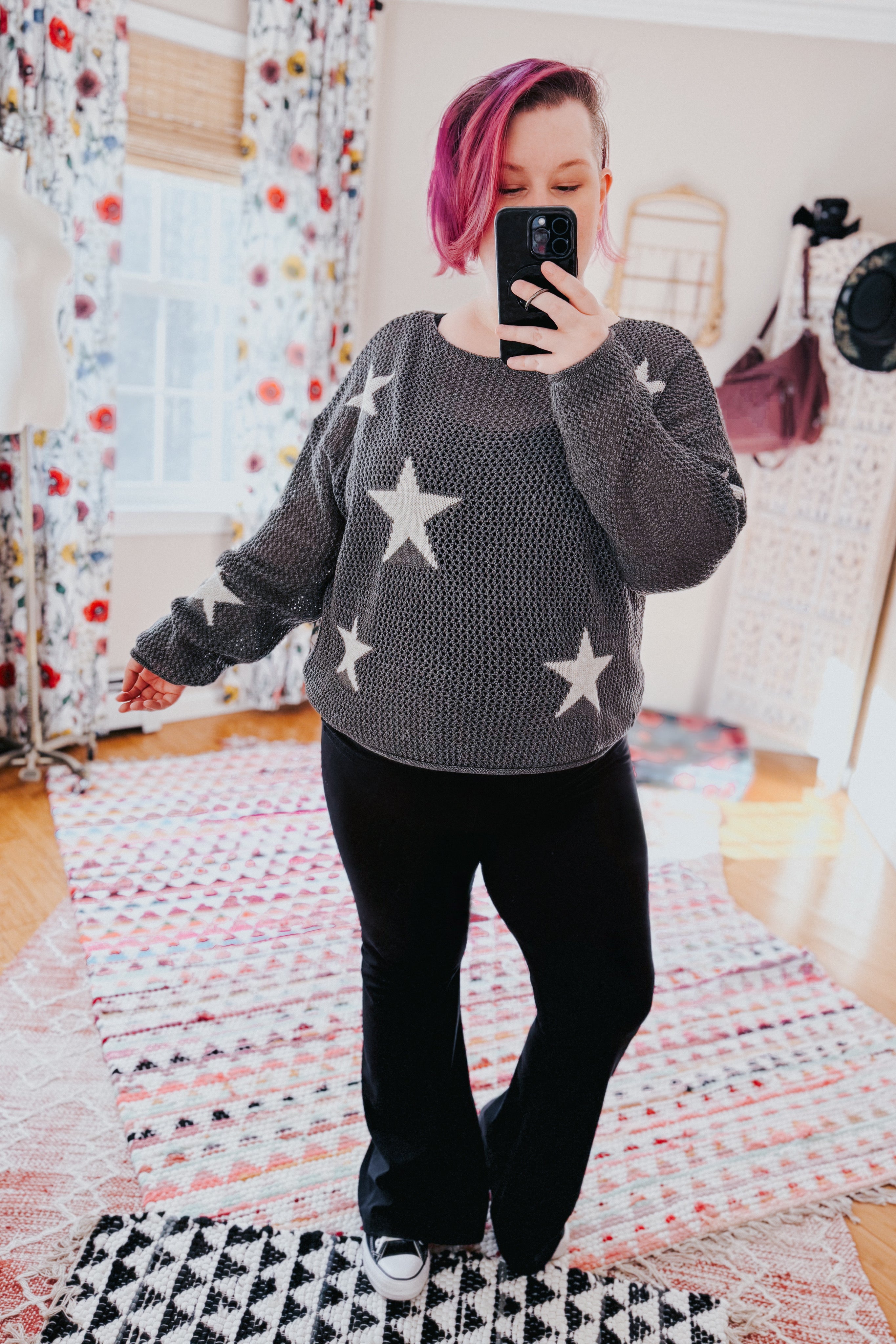 Woman wearing charcoal mesh sweater with star patterns paired with black pants and sneakers indoors