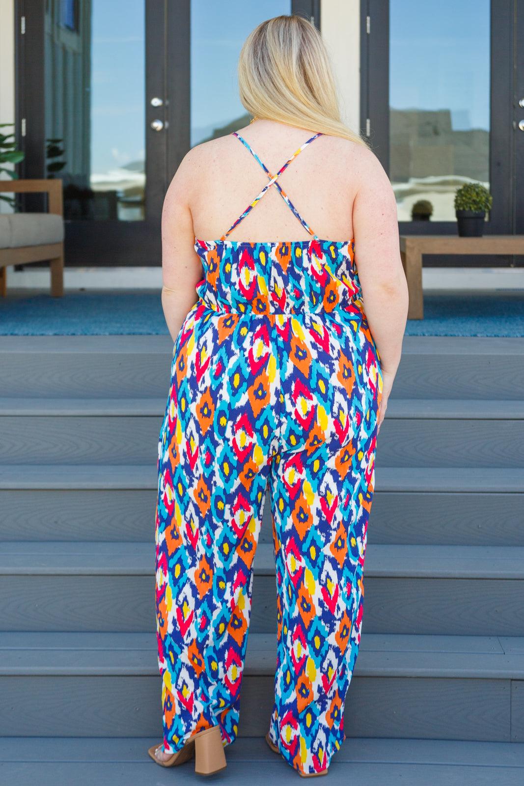Woman wearing colorful patterned jumpsuit with thin crossed straps standing on outdoor steps facing away