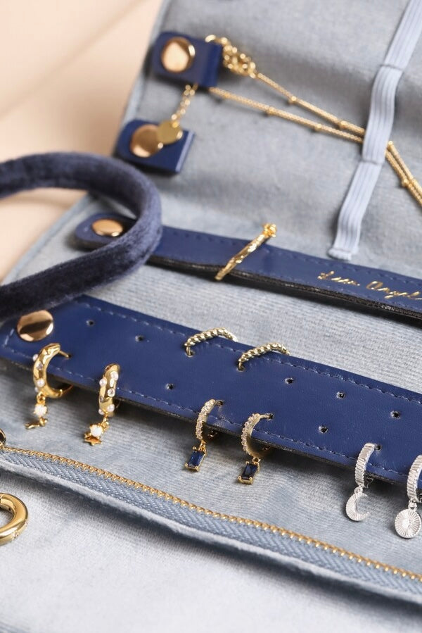 Close-up of cream velvet roll with navy blue straps holding delicate gold celestial-themed earrings and necklaces