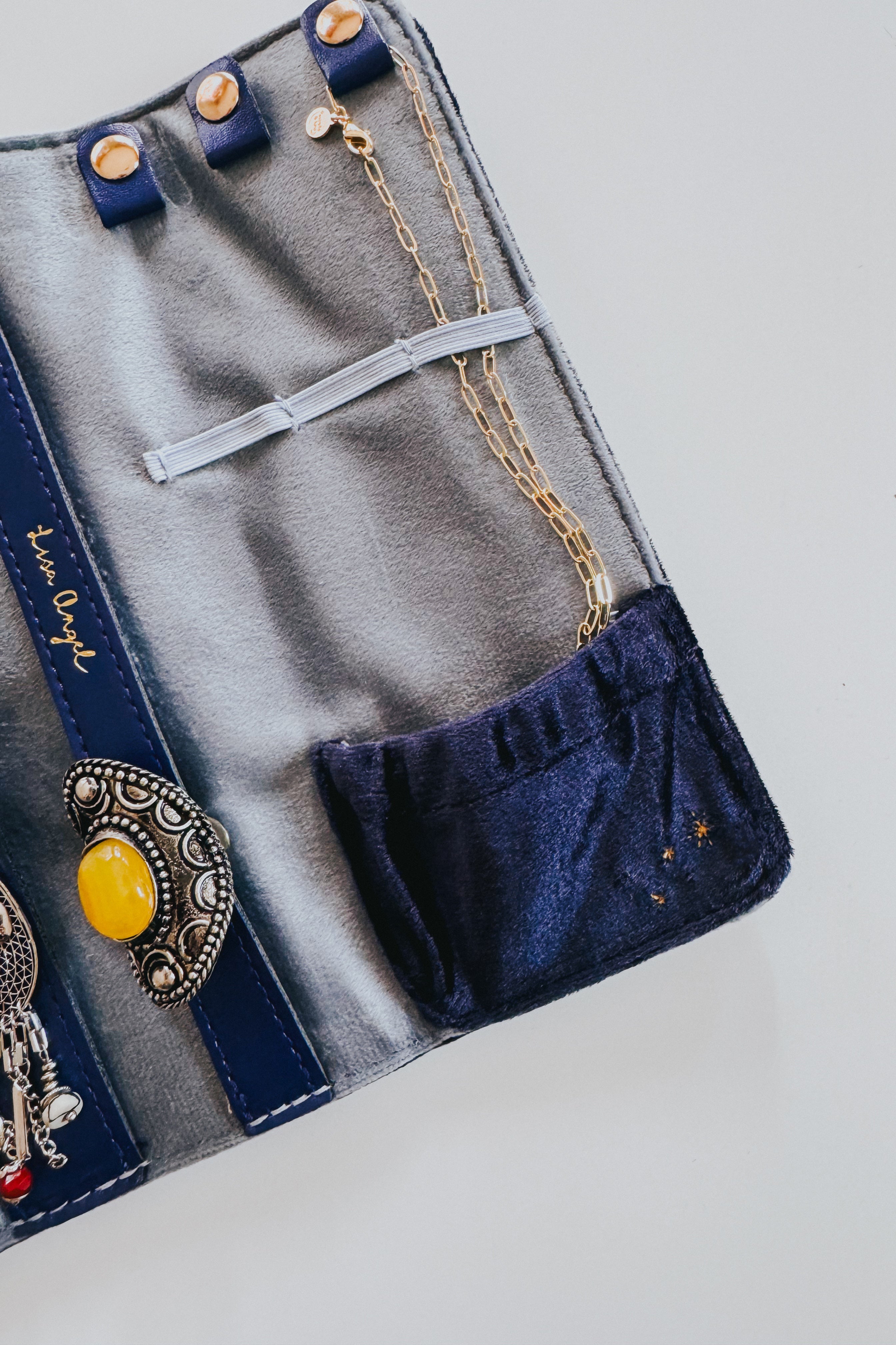 Open blue and navy velvet jewelry roll with gold chain and decorative silver and yellow jewelry inside